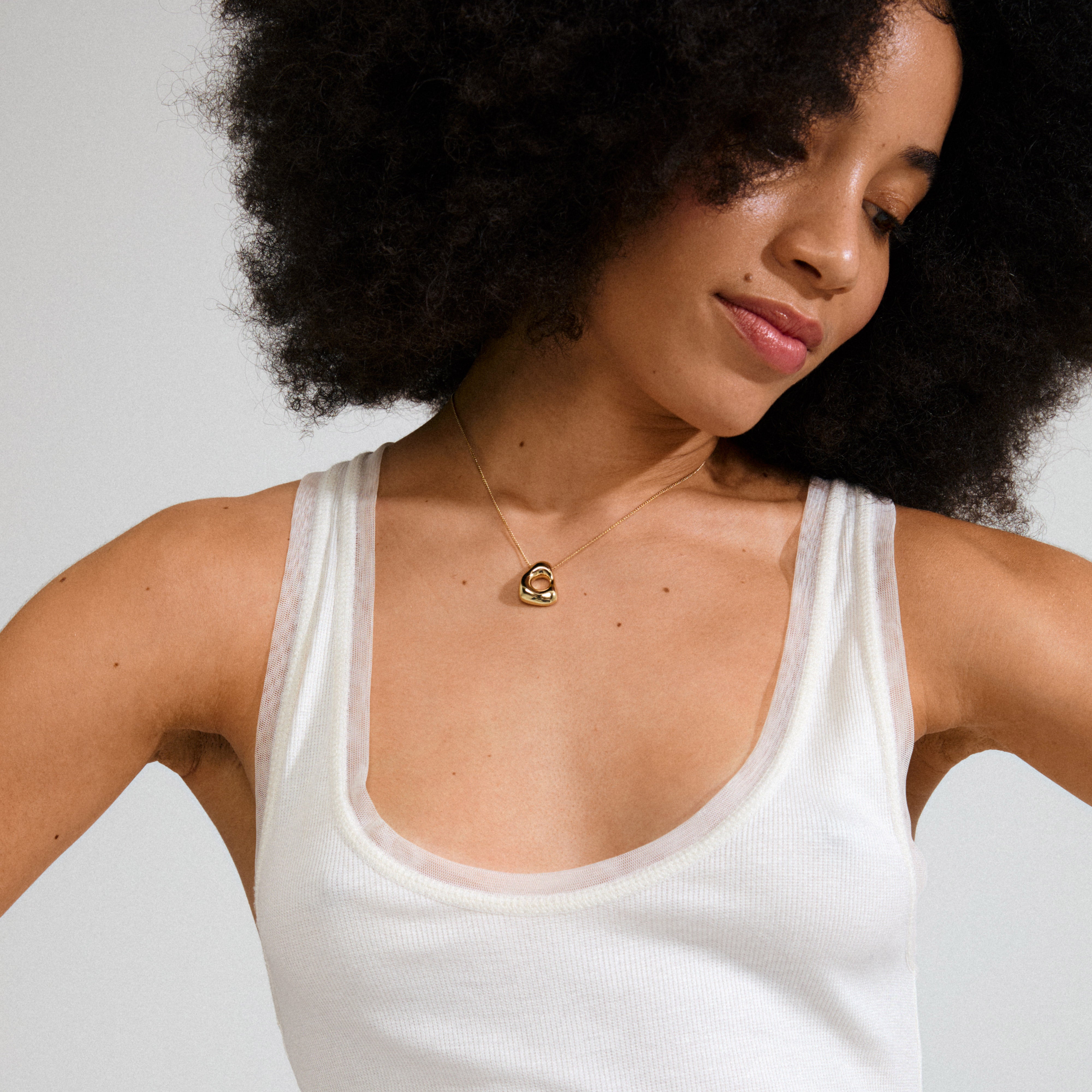 Woman wearing Pilgrim's FREE necklace gold-plated, featuring an abstract heart-shaped pendant on a delicate chain, embodying minimalist elegance and natural inspiration.