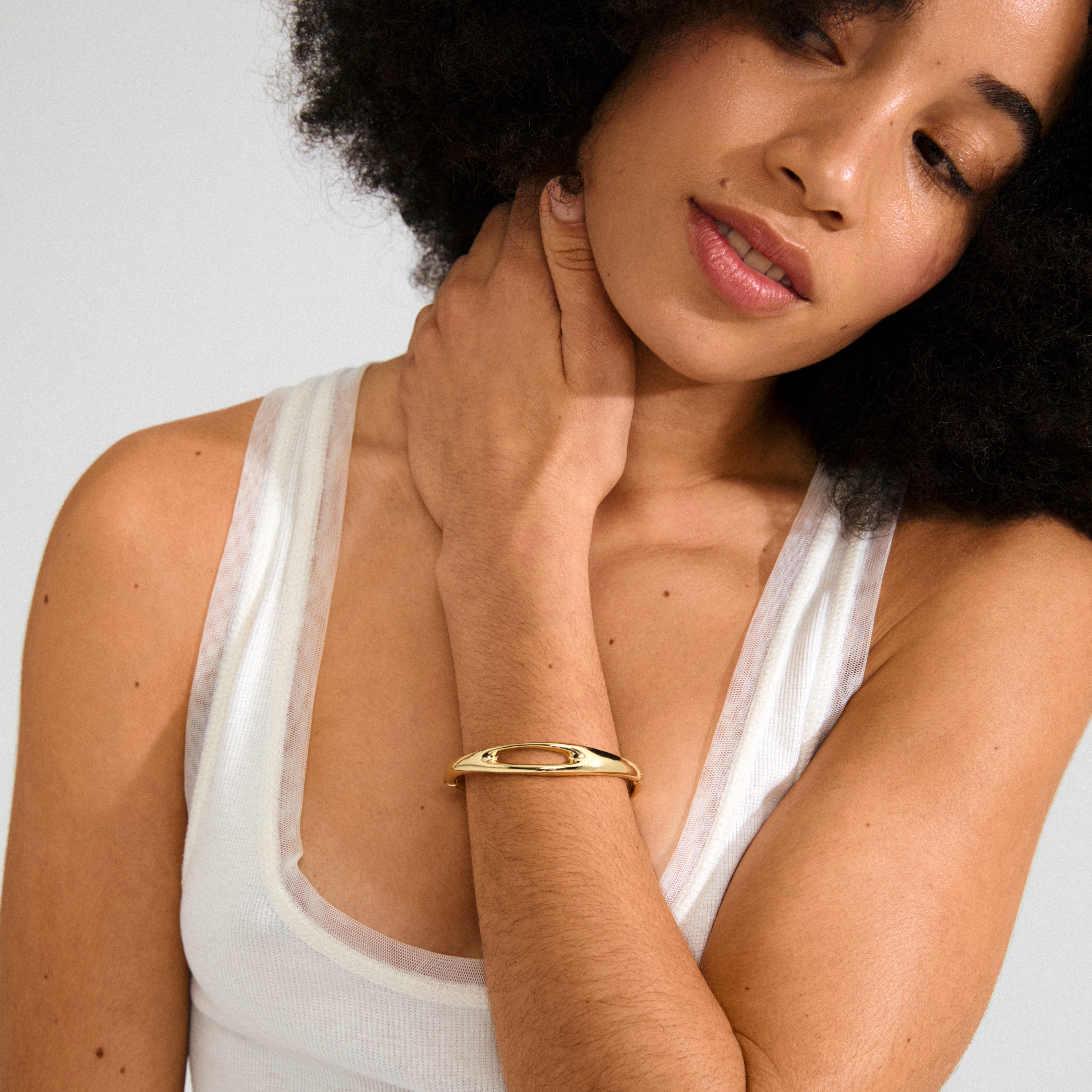 Young woman wears a white tank top and Pilgrim's gold-plated FREE bangle with unique cut-out design, showcasing Scandinavian-inspired elegance and simplicity.