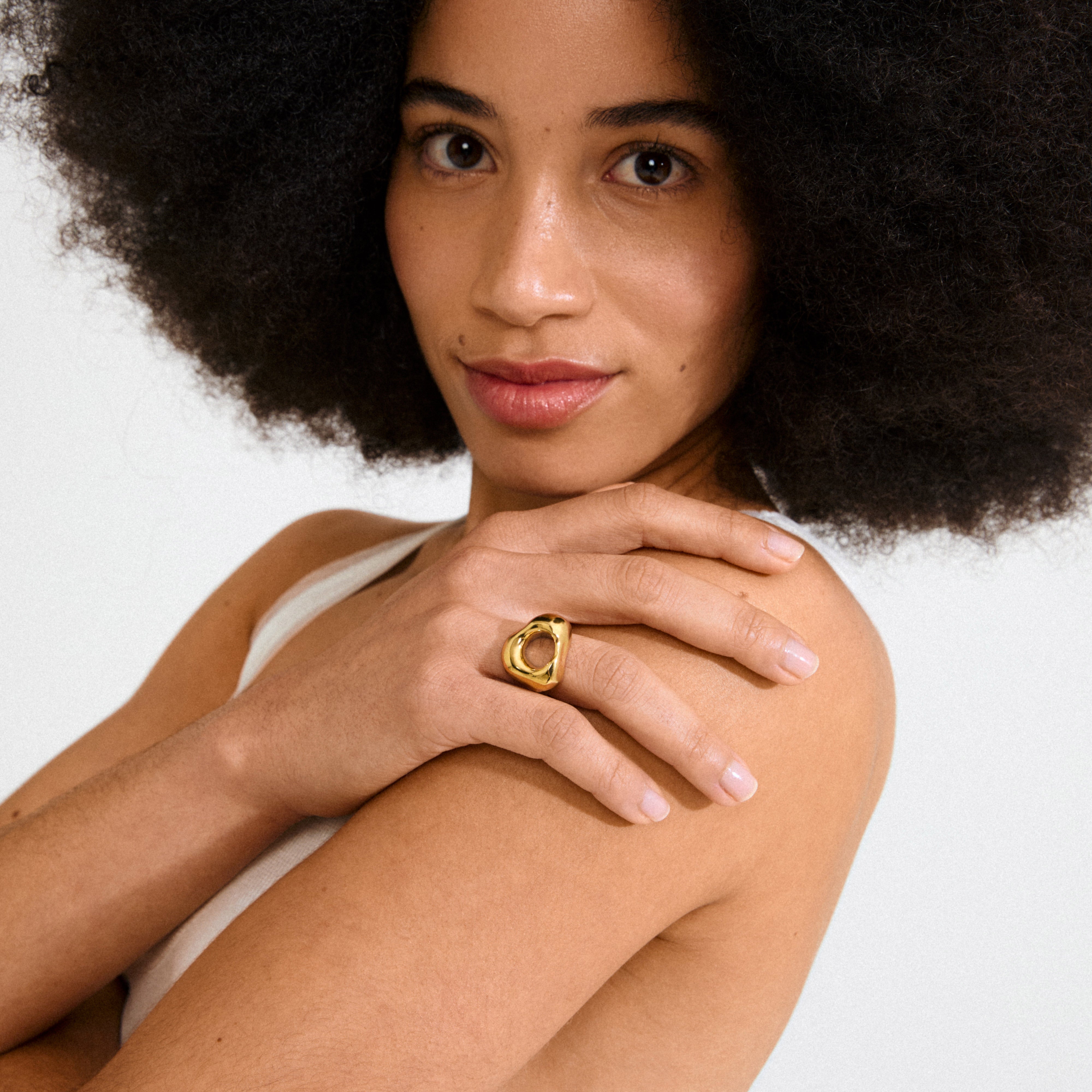 Young woman with an afro displays Pilgrim's FREE ring gold-plated on her finger, showcasing its chunky, organic design in a minimalist, natural-lit setting.