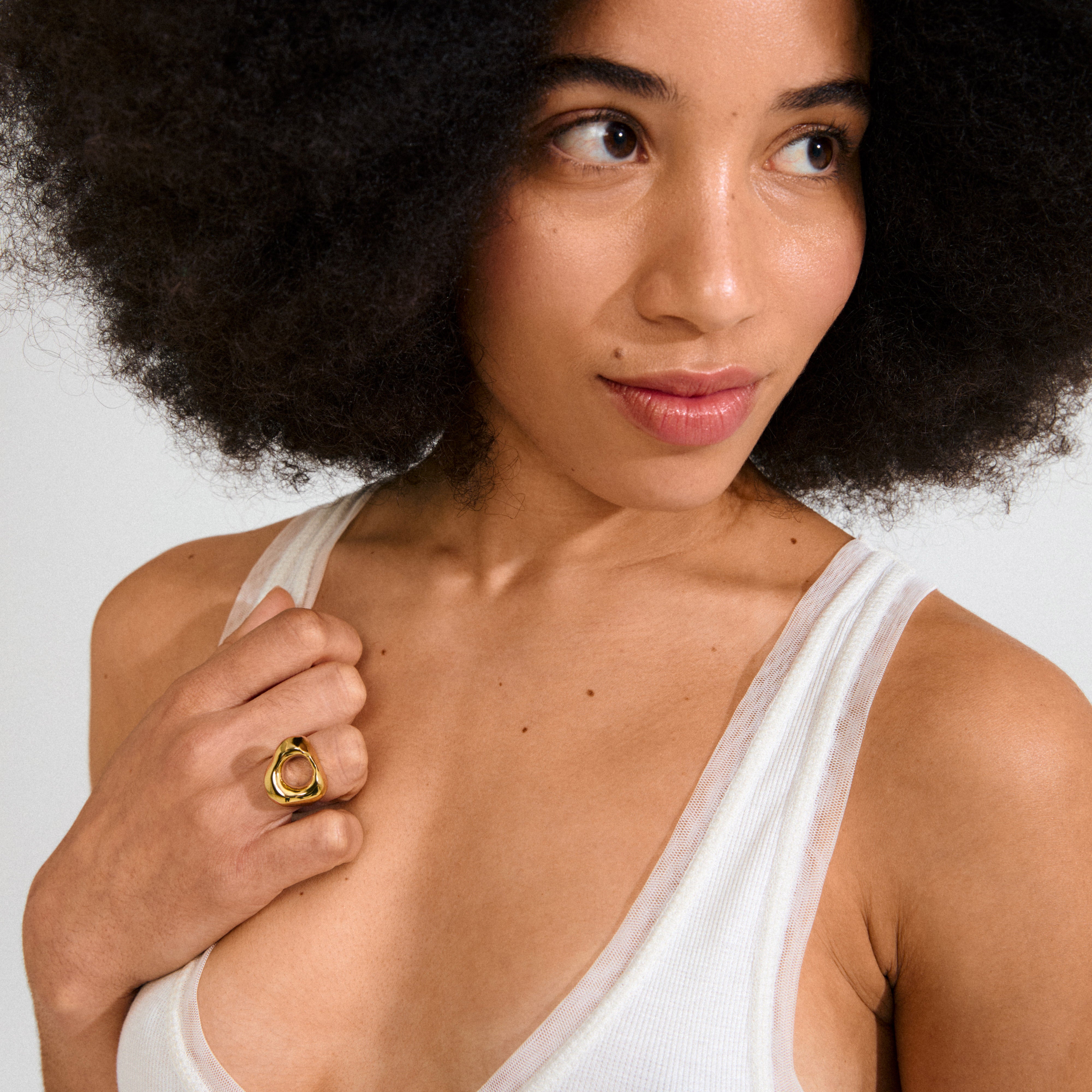 Woman with natural afro wears white tank top and Pilgrim's FREE ring gold-plated, featuring an abstract, organic design, inspired by natural beach stones.