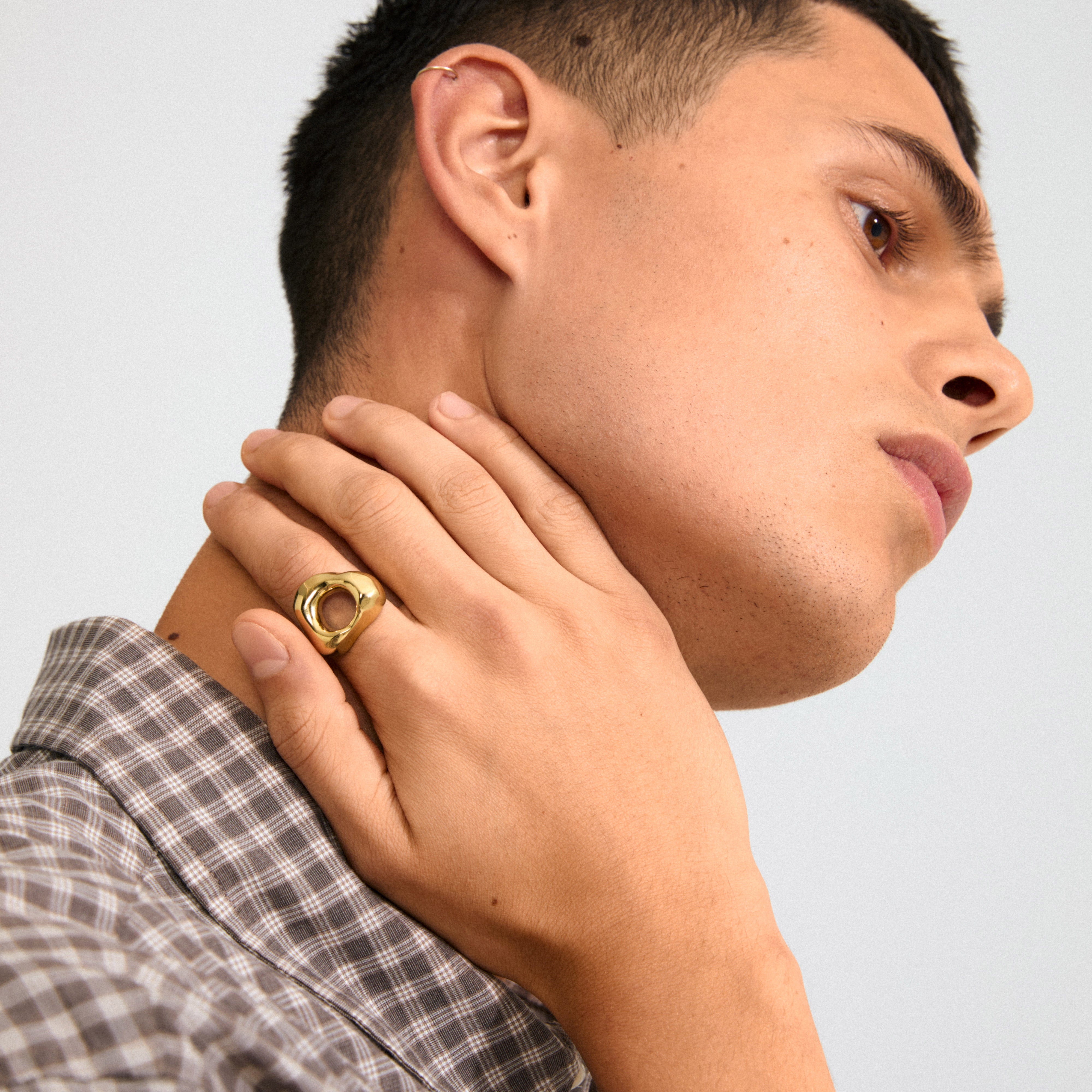 Young man wearing Pilgrim's FREE gold-plated ring with an organic design, inspired by natural forms, highlighted against his neck, paired with a small hoop earring.