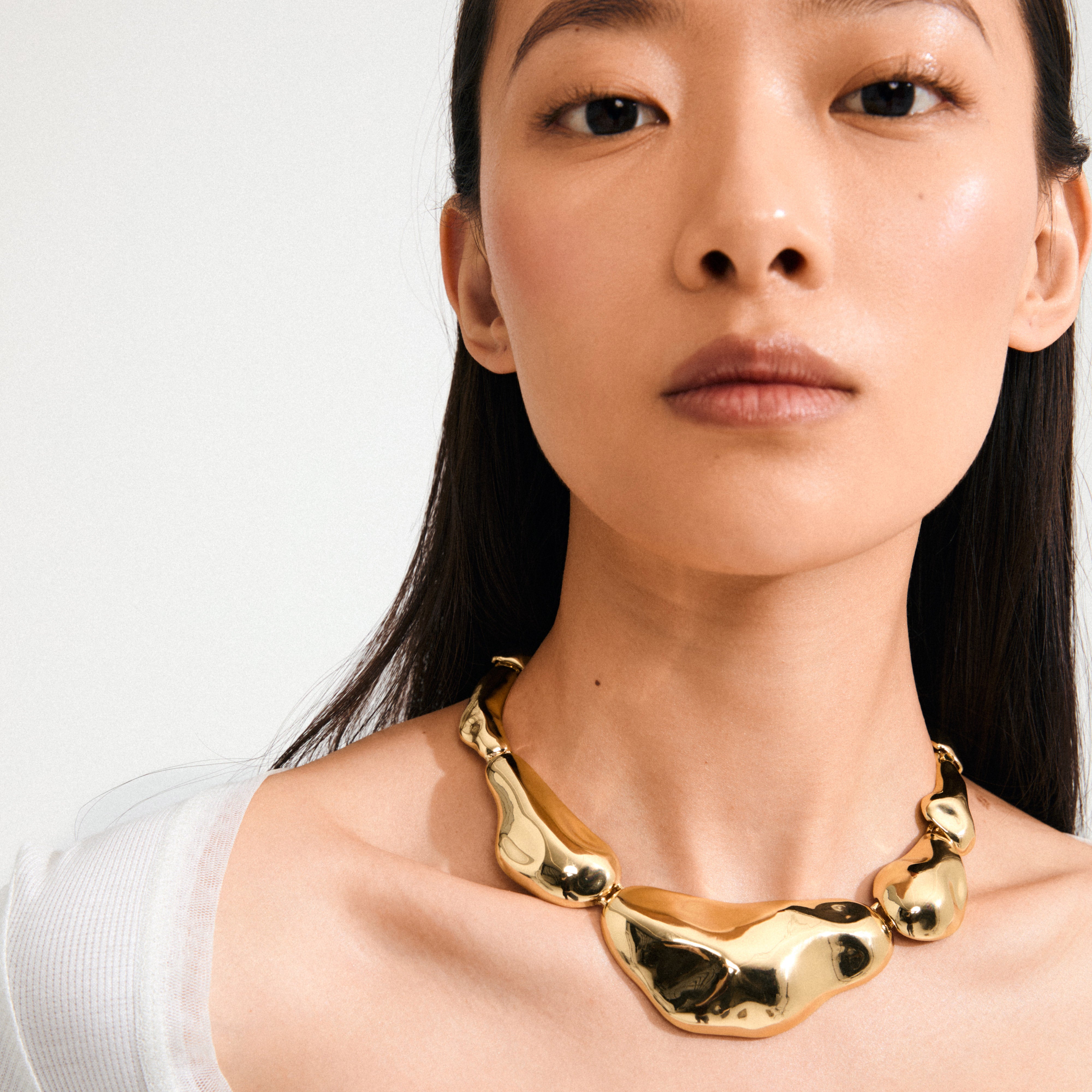 Young woman wearing Pilgrim's FREE statement necklace, a chunky gold-plated piece with asymmetrical segments, capturing light and standing out as a stylish, recycled accessory.