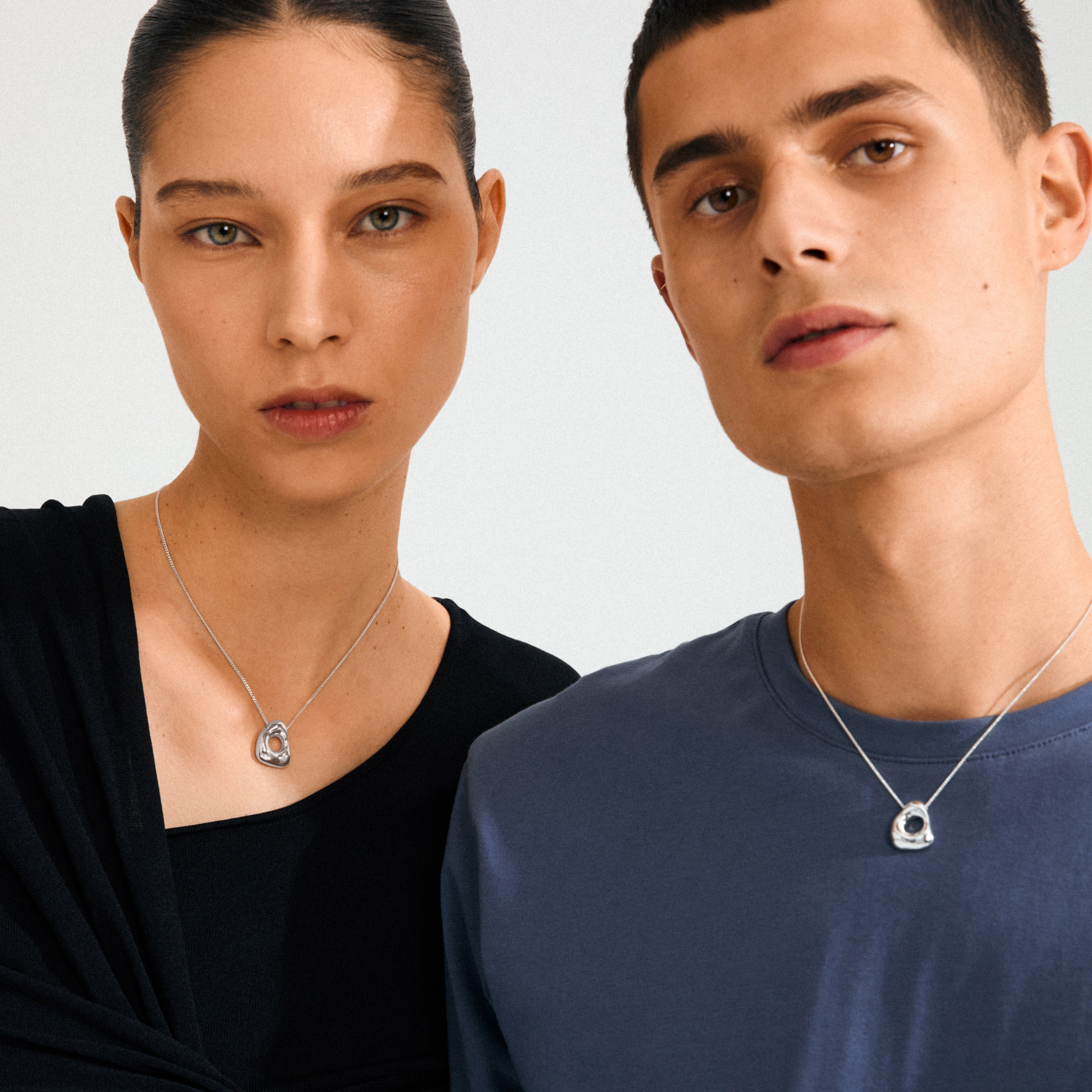Two people wearing Pilgrim's silver-plated FREE necklace, featuring abstract circle pendants with beads, inspired by ocean waves and beach pebbles.