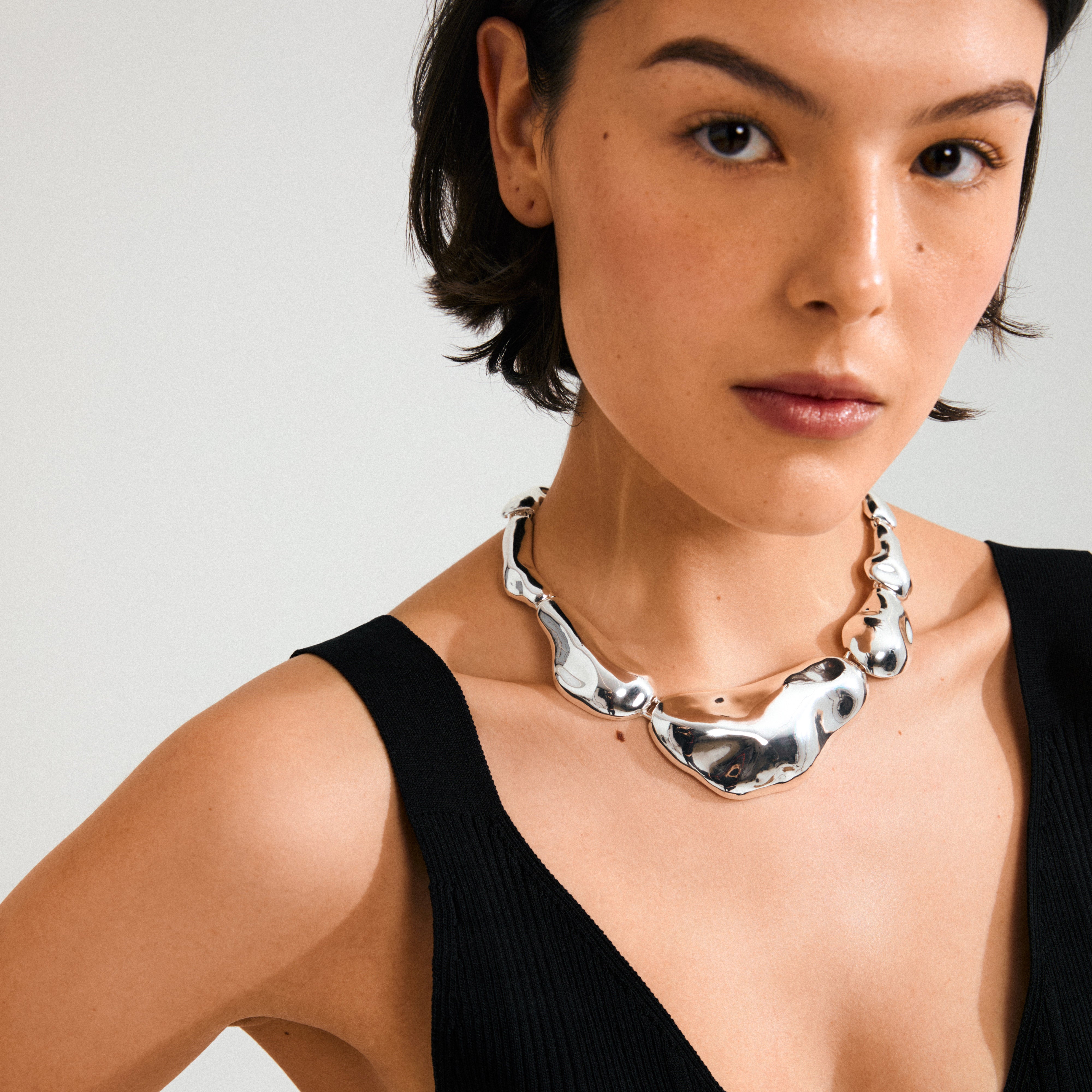 Young woman wearing Pilgrim's FREE statement necklace, a silver-plated piece with irregular, mirror-like links, embodying playful ocean-inspired elegance.