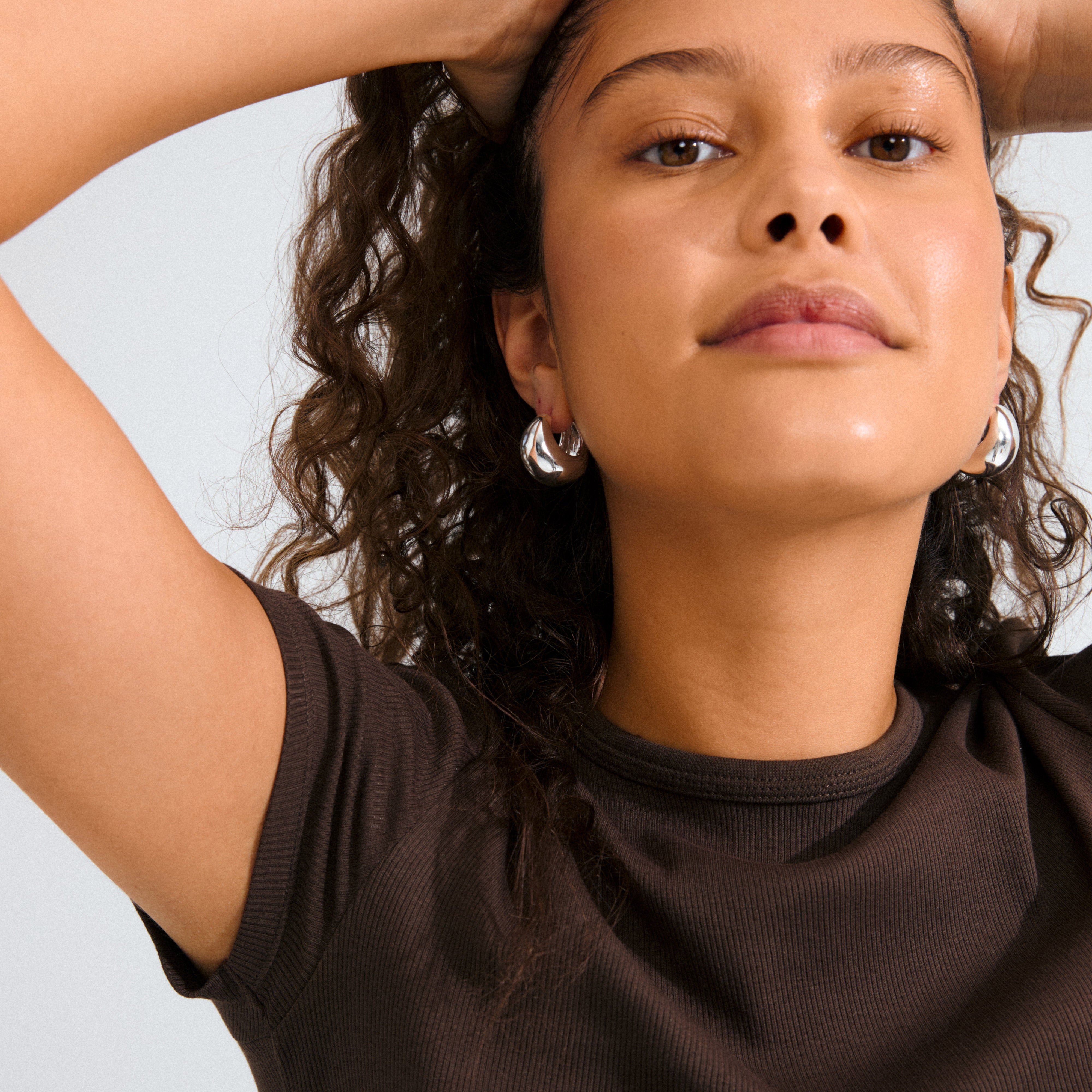 Person with curly hair wearing Pilgrim's FREE hoops, silver-plated chunky earrings, showcasing their shiny, uneven design for an effortlessly chic look.
