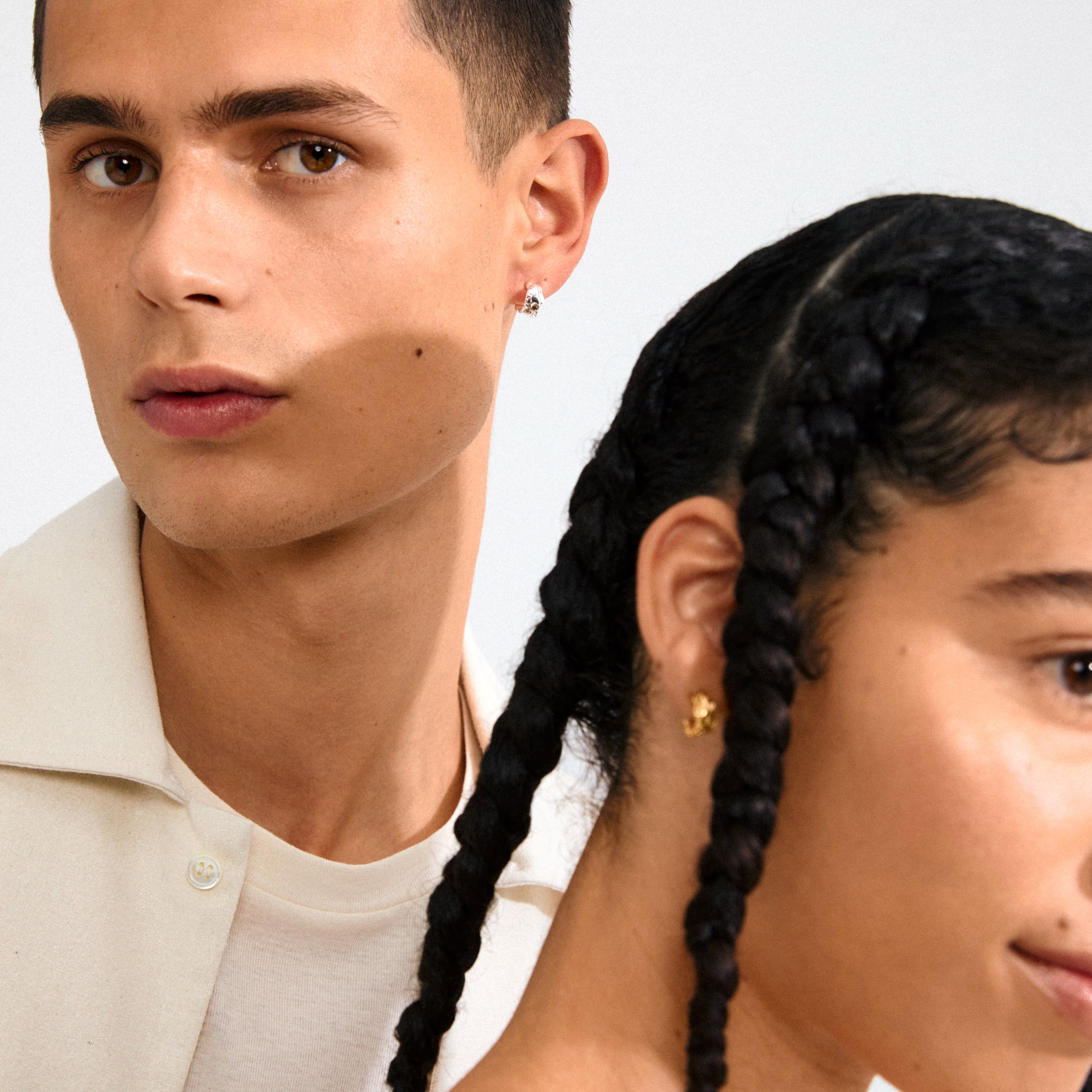 Two young adults showcase INSTANT earrings; a woman's profile displays the gold-plated semi-hoop, highlighting its shiny, organic texture and minimalist elegance.