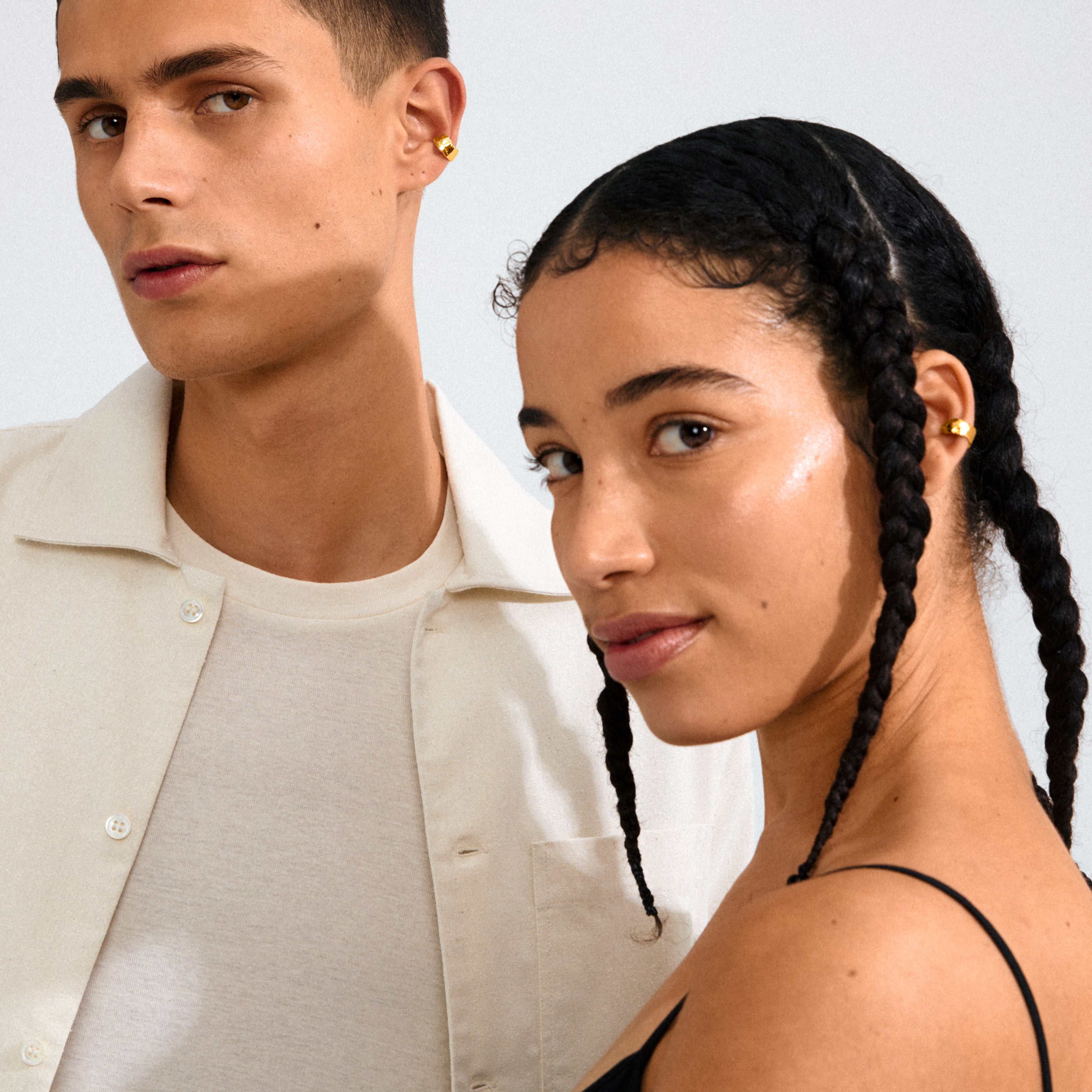 Two models showcase Pilgrim's INSTANT ear cuff, a gold-plated, hammered-texture piece for a chic, minimalist look. Both wear the cuff stylishly on one ear.