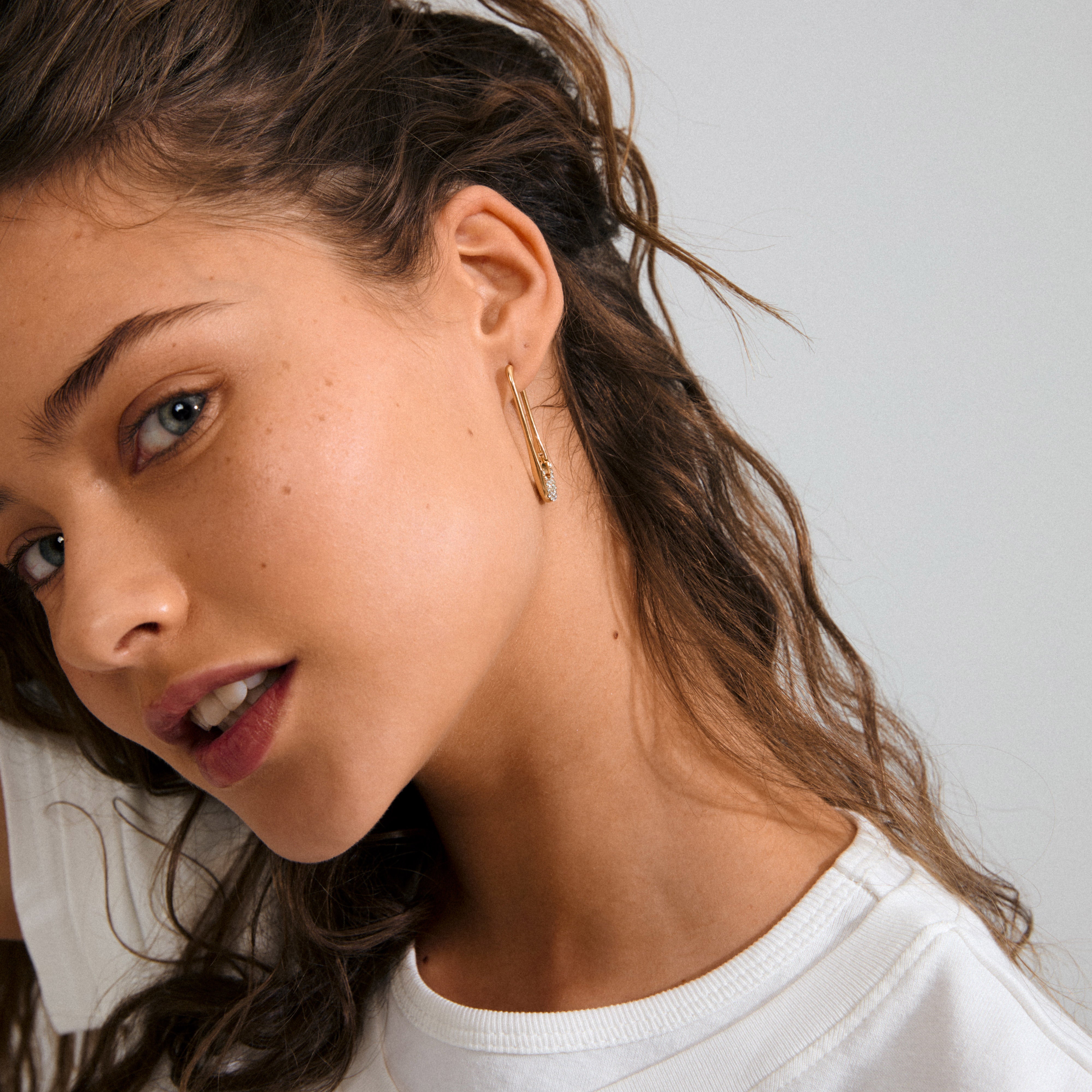 Young woman wearing Pilgrim's INSTANT hoops gold-plated earrings, featuring a sleek design with a small gemstone, embodying a blend of edgy and luxurious style.