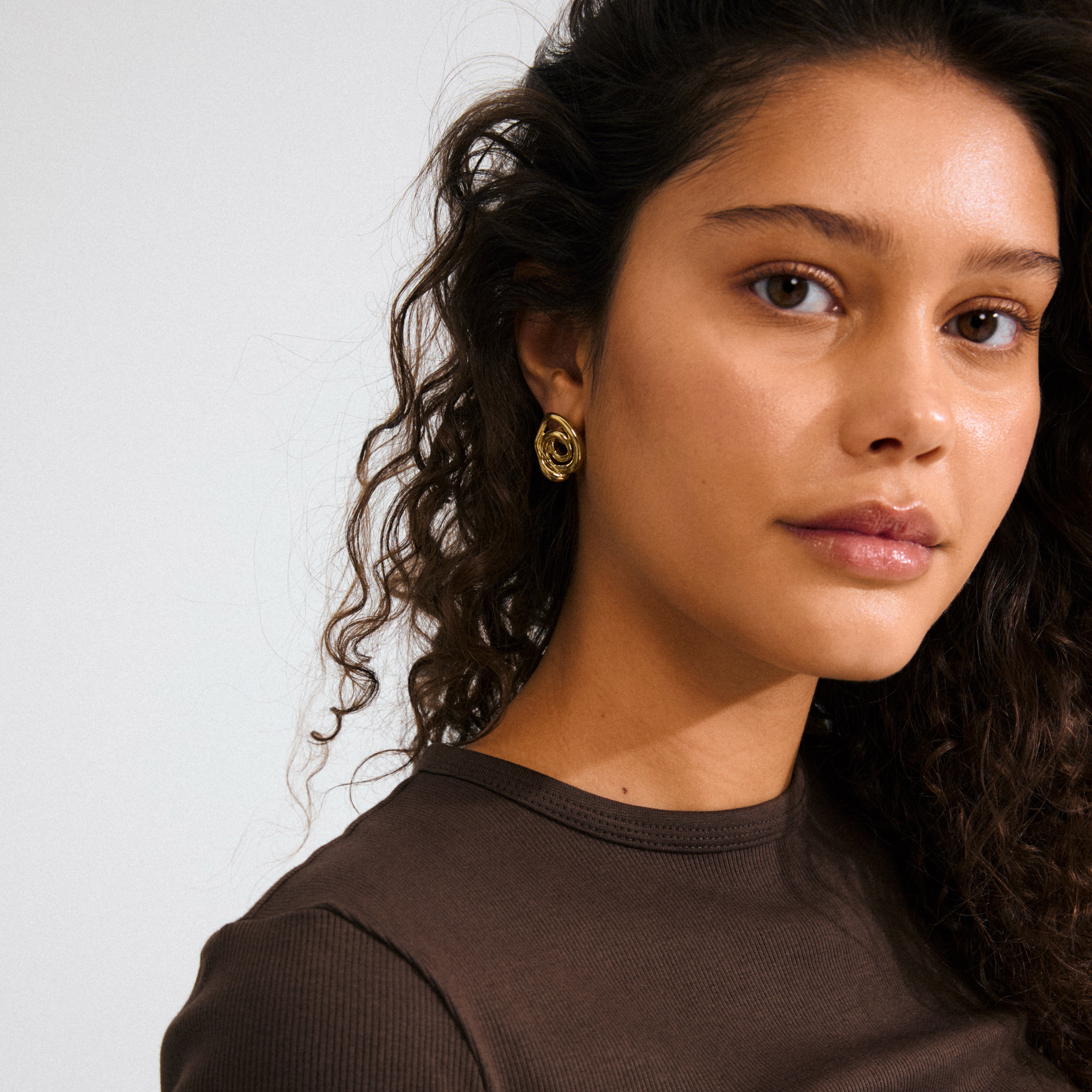 Gold-plated UNFOLD earring on woman with curly hair, showcasing its spiral, doodle design. A playful, artistic piece embodying Pilgrim's trendy, inclusive style.