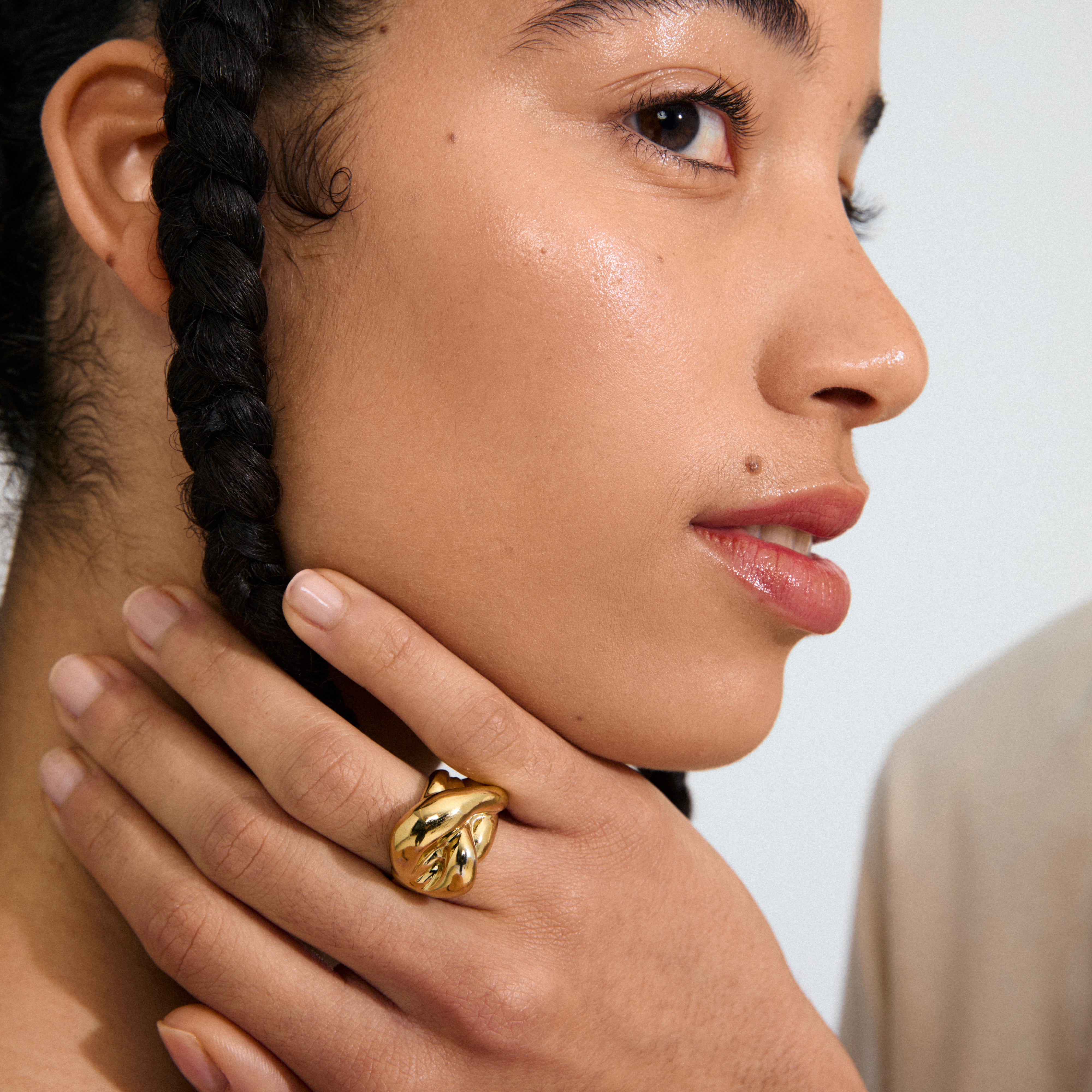 Profile view of a young person wearing the gold-plated UNFOLD ring by Pilgrim, showcasing its sculptural, organic design on their middle finger.