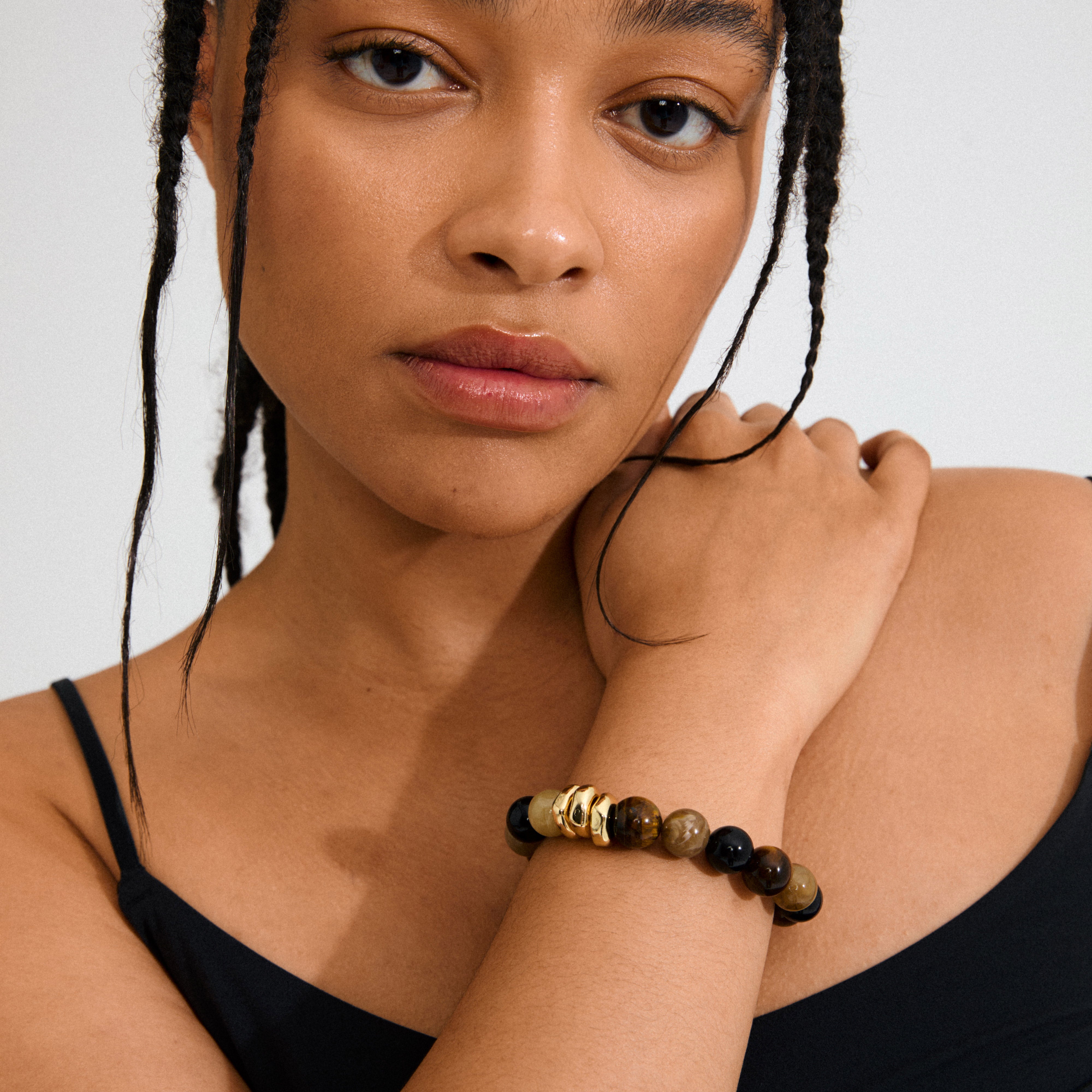 UNFOLD bracelet gold-plated/brown on woman's wrist, featuring tiger-eye beads and gold-plated rings, accentuating a modern, confident style.