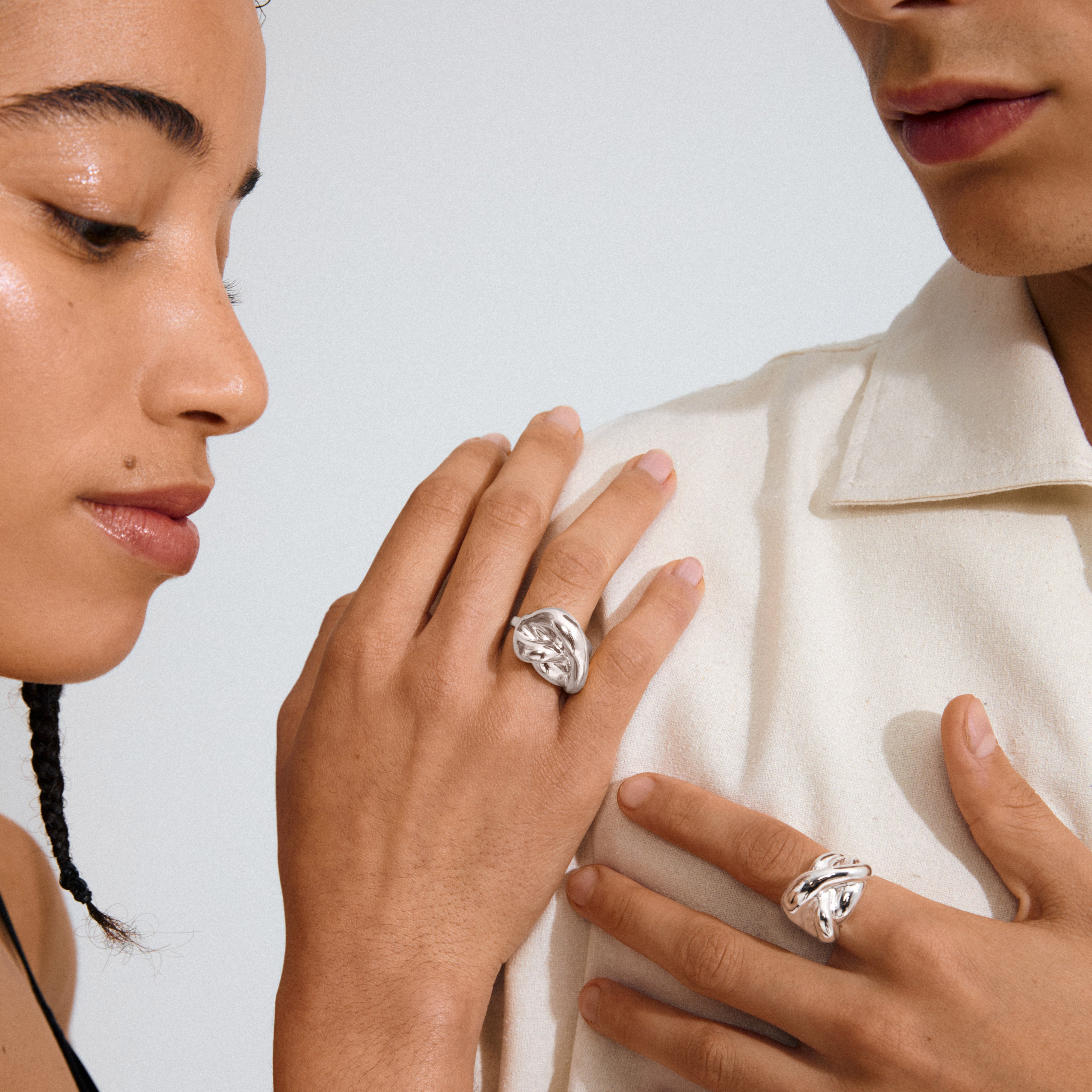 Two hands adorned with Pilgrim's UNFOLD silver-plated rings, showcasing their fluid, organic design and sculptural elegance, emphasizing artistic energy and personal style.