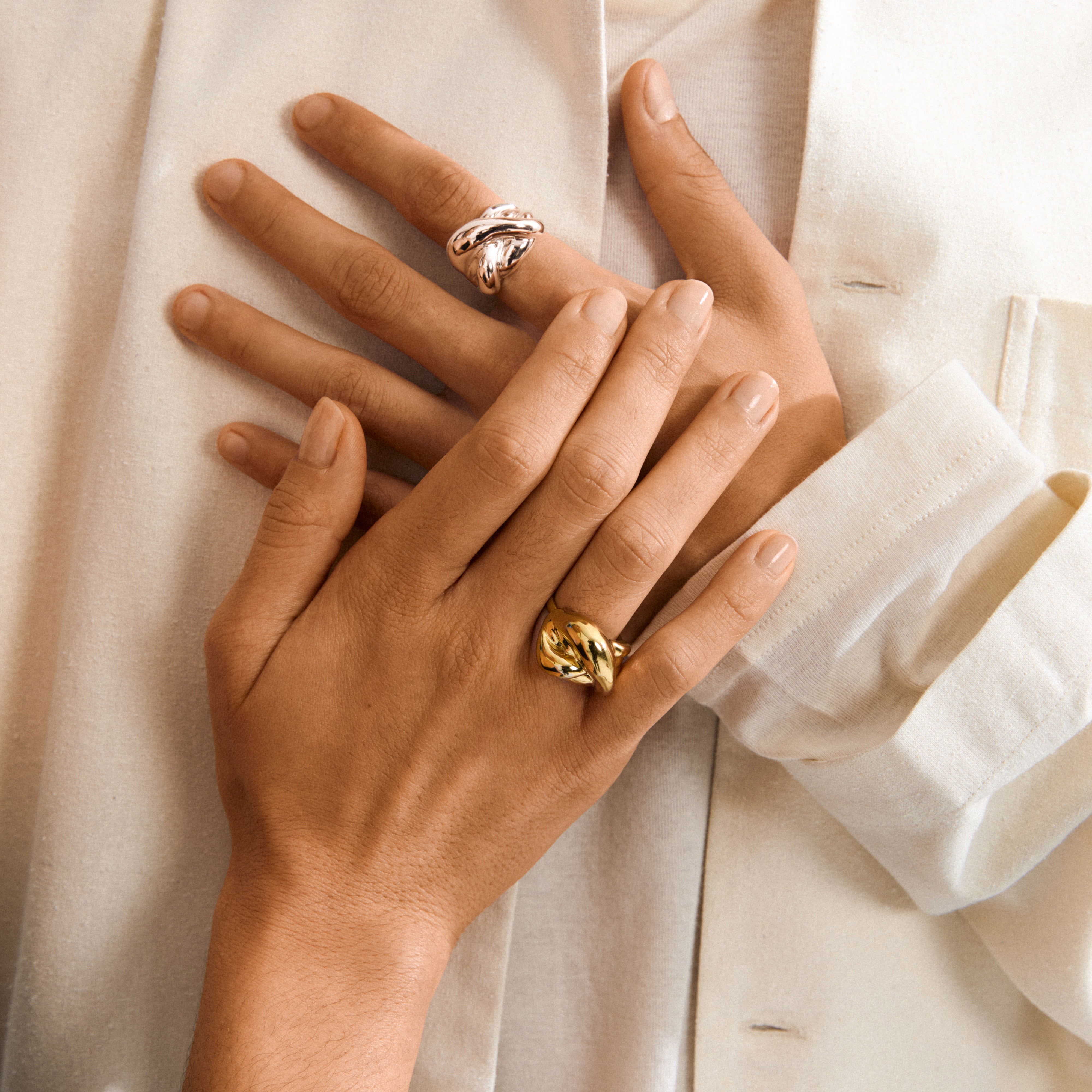 Hands wearing sculptural UNFOLD ring silver-plated by Pilgrim, showcasing its organic, twisted design on soft fabric, embodying artistic energy and stylish flexibility.