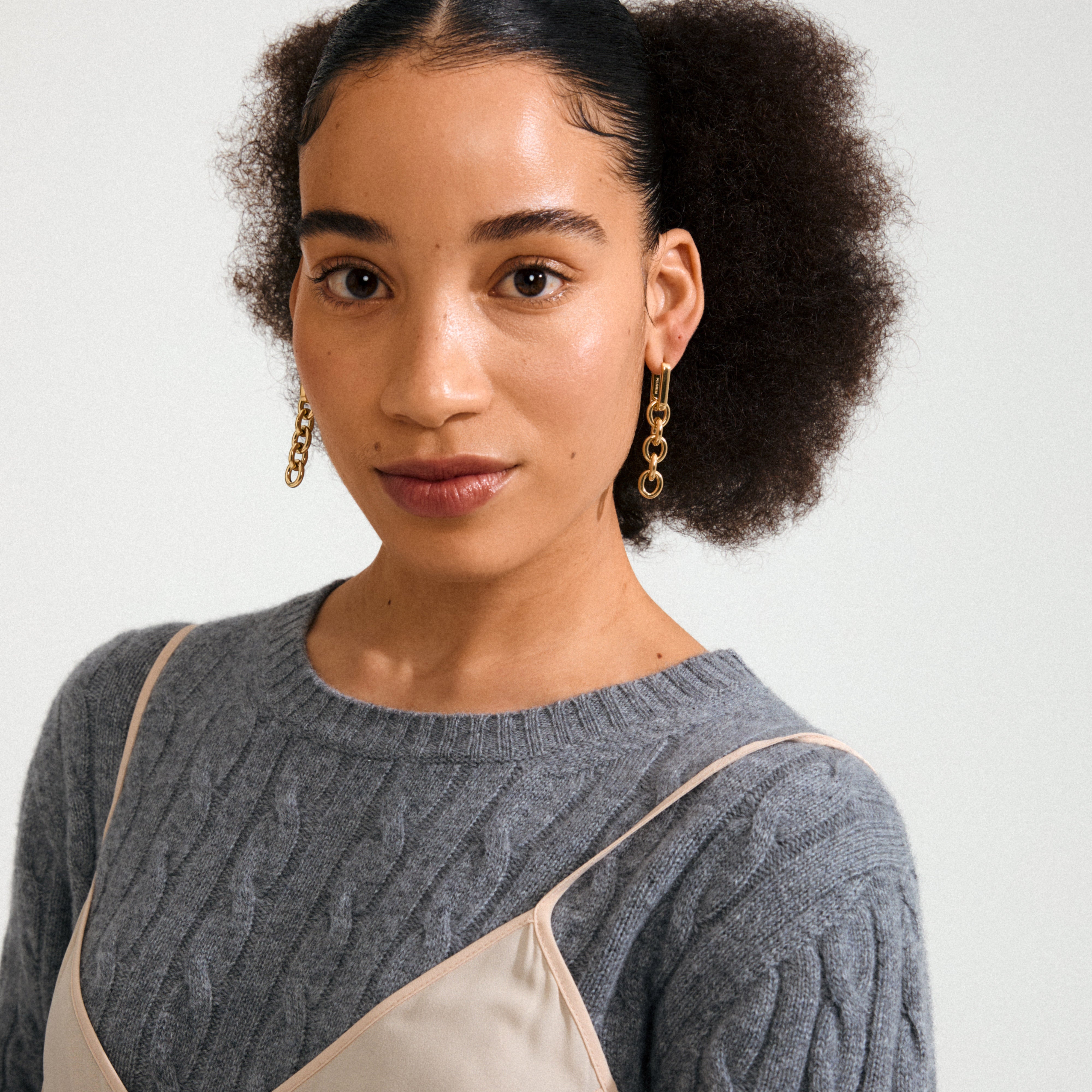 Close-up of Pilgrim's PHASE earrings gold-plated, featuring short gold chains, worn by a person with natural hair, embodying urban style and classic elegance.