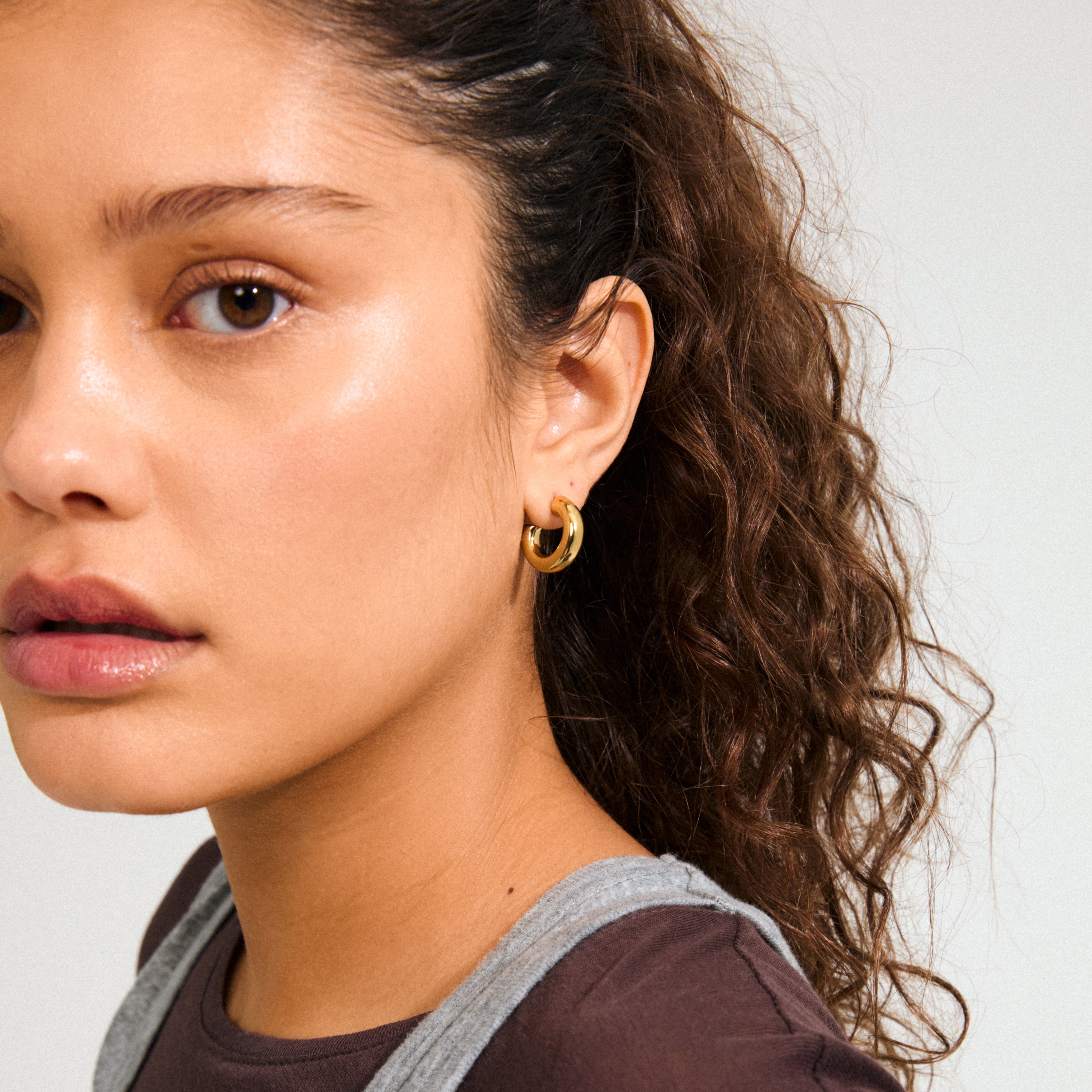 Young person wearing Pilgrim's PHASE small gold-plated hoops, showcasing a chunky silhouette for a refined, autumn-ready look, embodying quiet luxury and crafted from recycled materials.