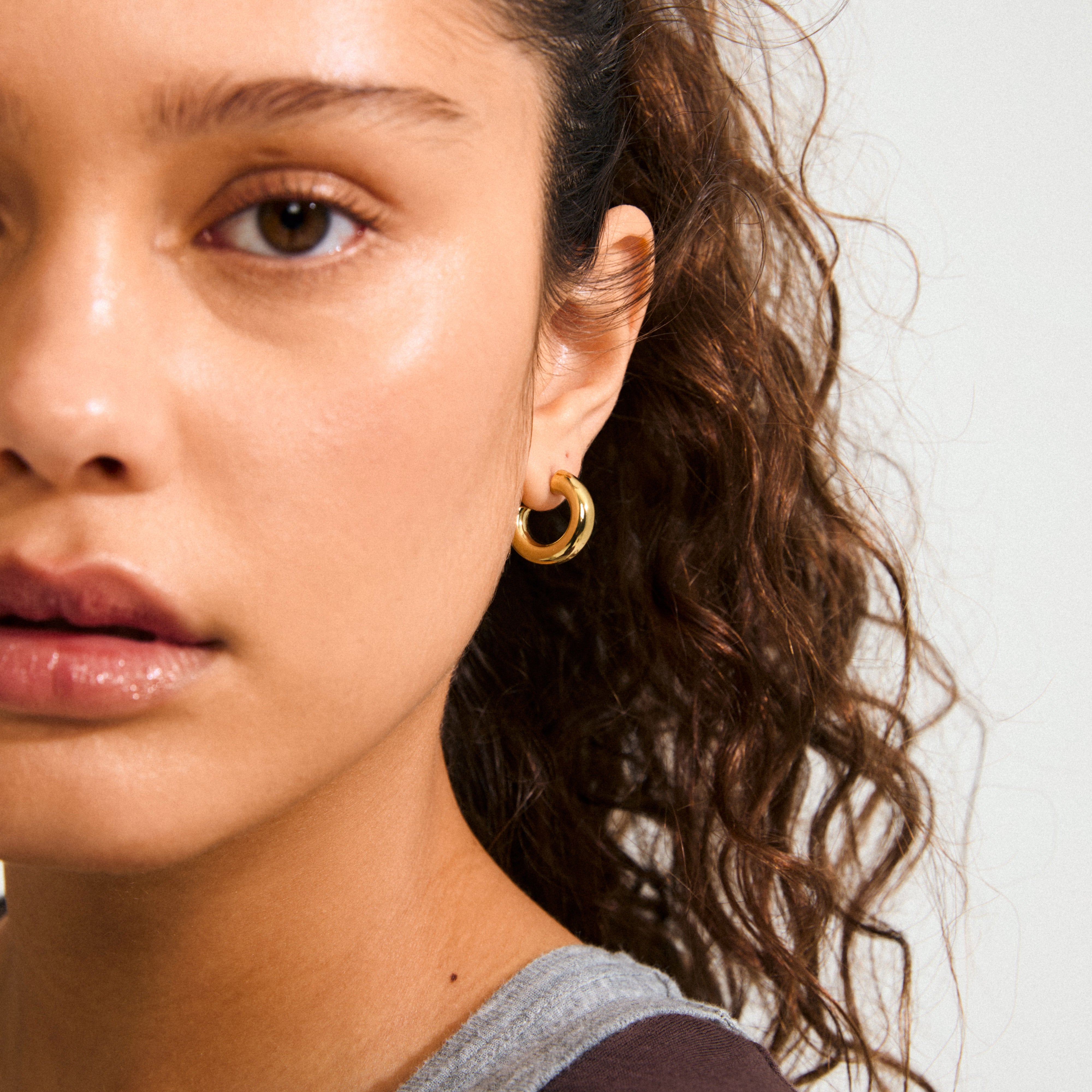 Close-up of a young woman wearing PHASE small hoops gold-plated, showcasing their chunky design and elegant finish. Ideal for a refined and stylish look.