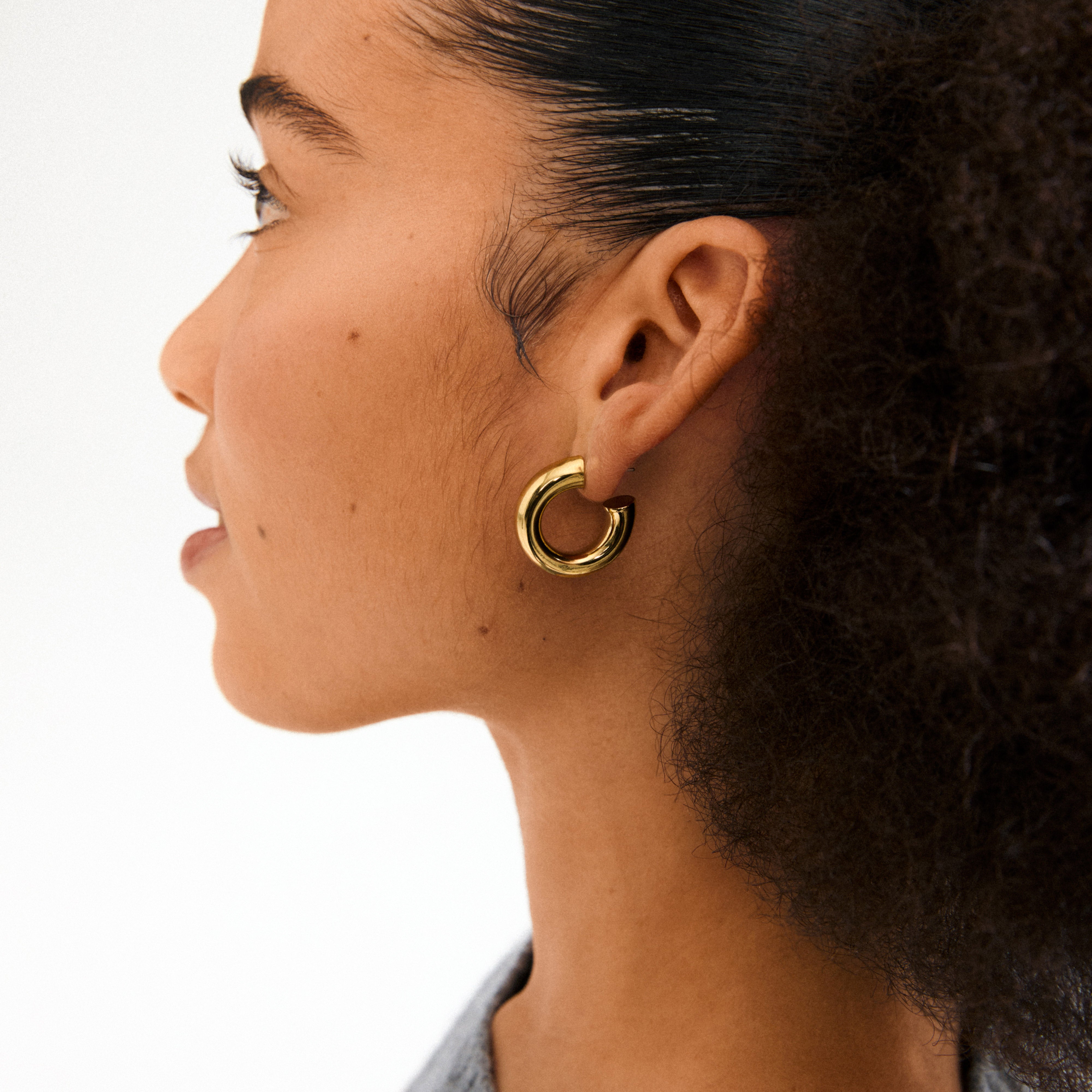 Side profile highlighting PHASE large gold-plated hoops by Pilgrim, showcasing their chunky silhouette on an ear with dark, pulled-back hair.
