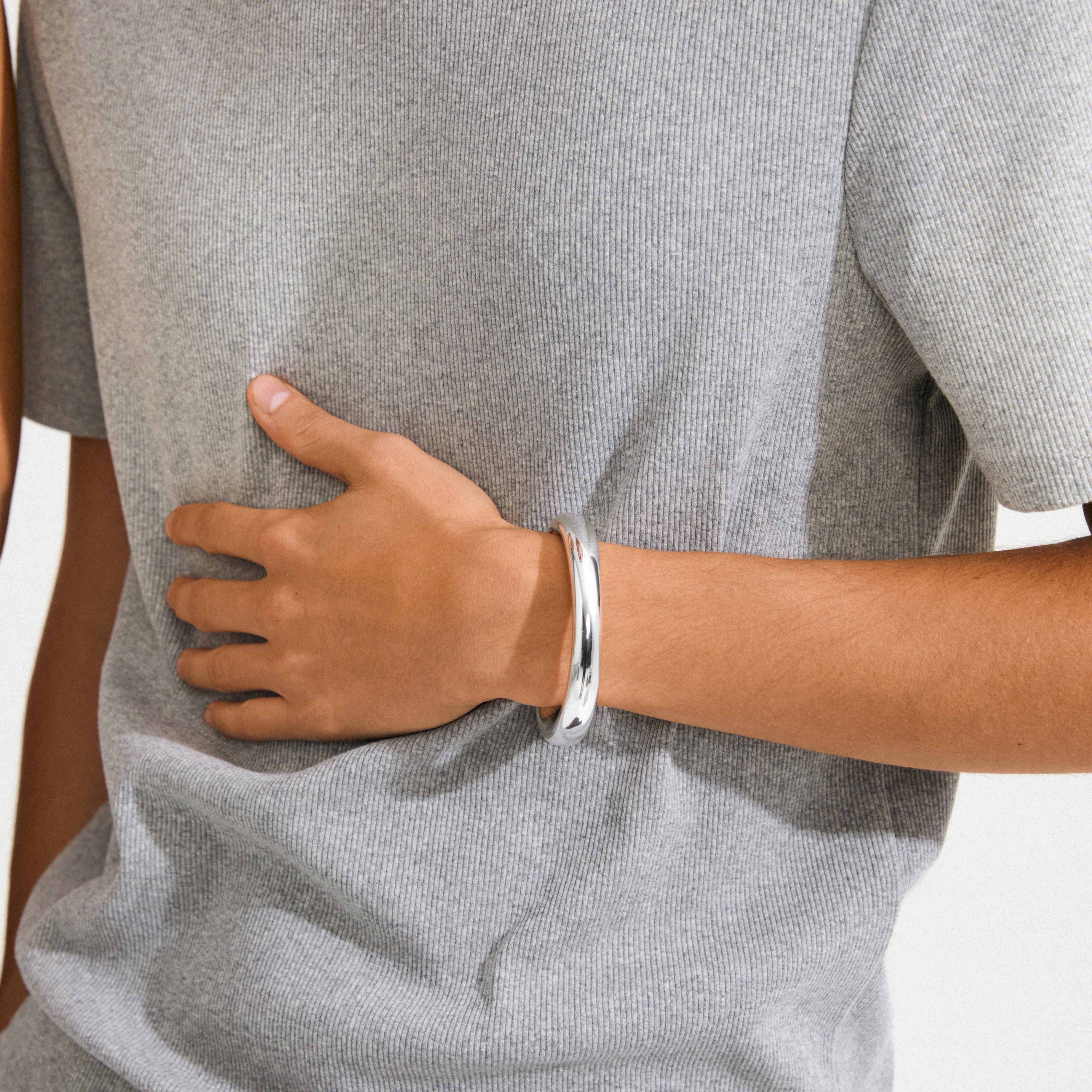 Person's midsection wearing a light grey T-shirt, showcasing Pilgrim's PHASE bangle silver-plated, a chunky, polished piece emphasizing sleek design and sustainable fashion.