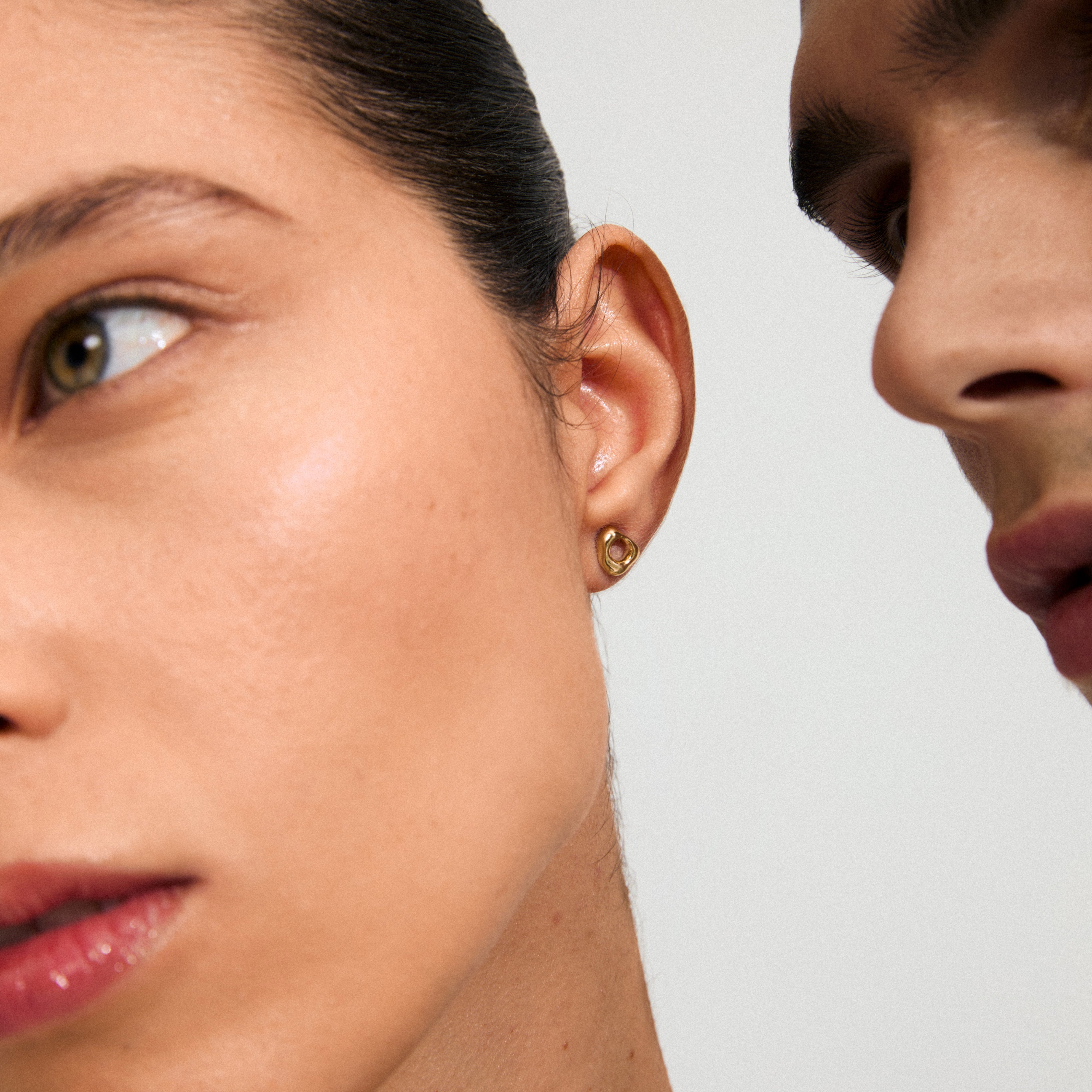 Gold-plated FREE stud earring, inspired by hagstones, shines in a close-up, emphasizing its organic shape on a woman's ear. Perfect for everyday wear.