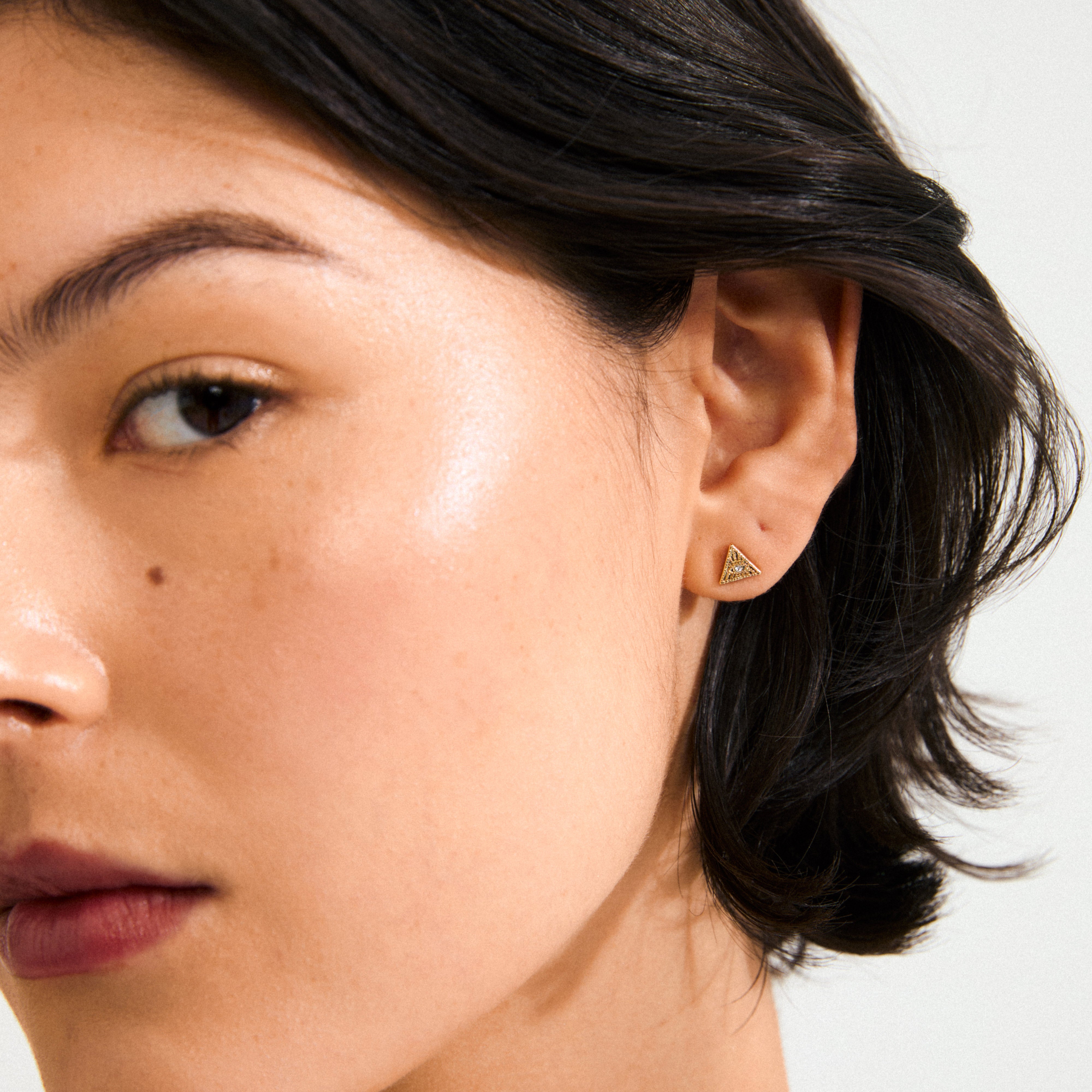 Close-up of a person's ear wearing RYLEE earrings gold-plated, triangle studs with tiny stones, adding boho chic to a minimalist look.