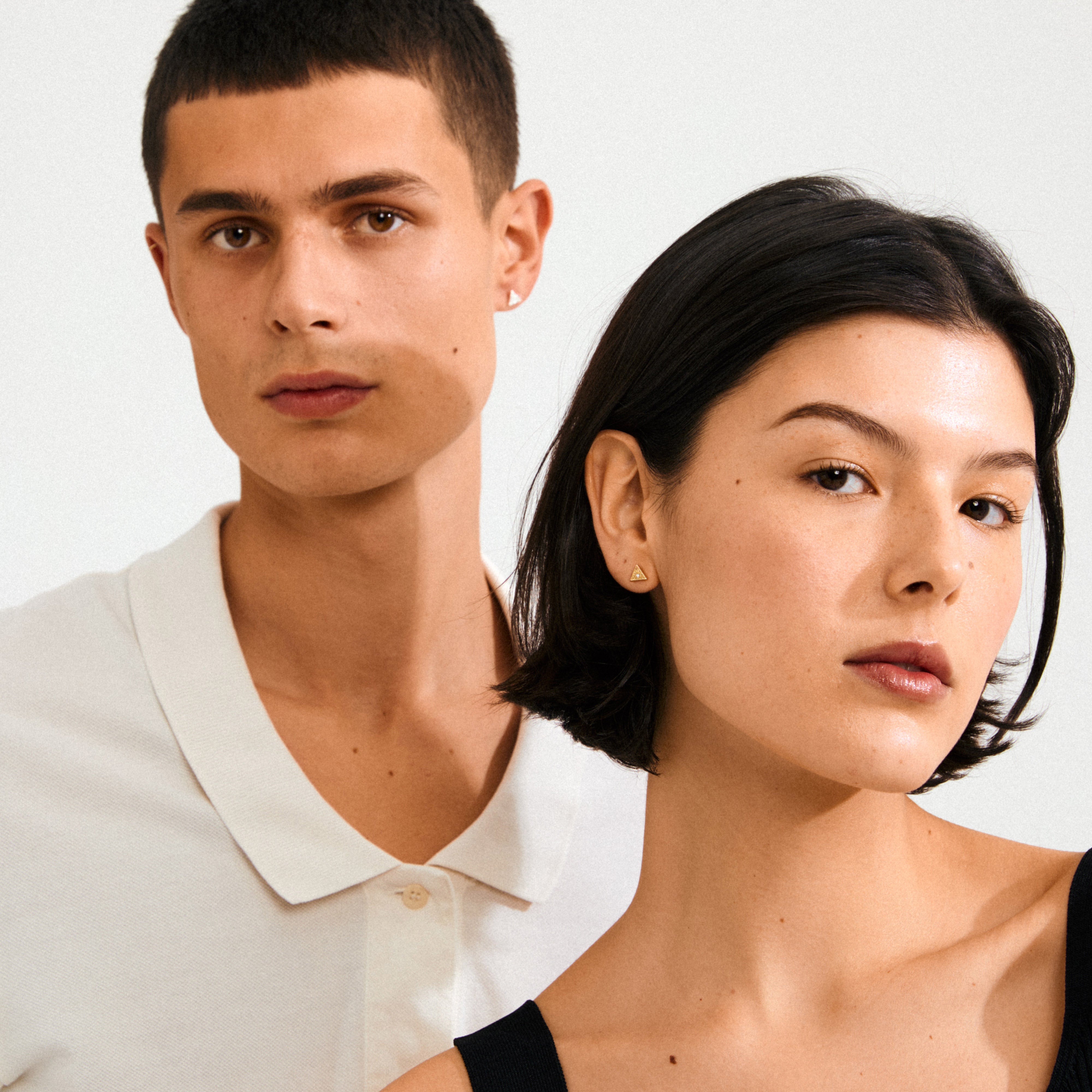 Close-up of a young man and woman wearing RYLEE gold-plated stud earrings, showcasing minimalist style with boho chic triangles featuring an all-seeing eye design.