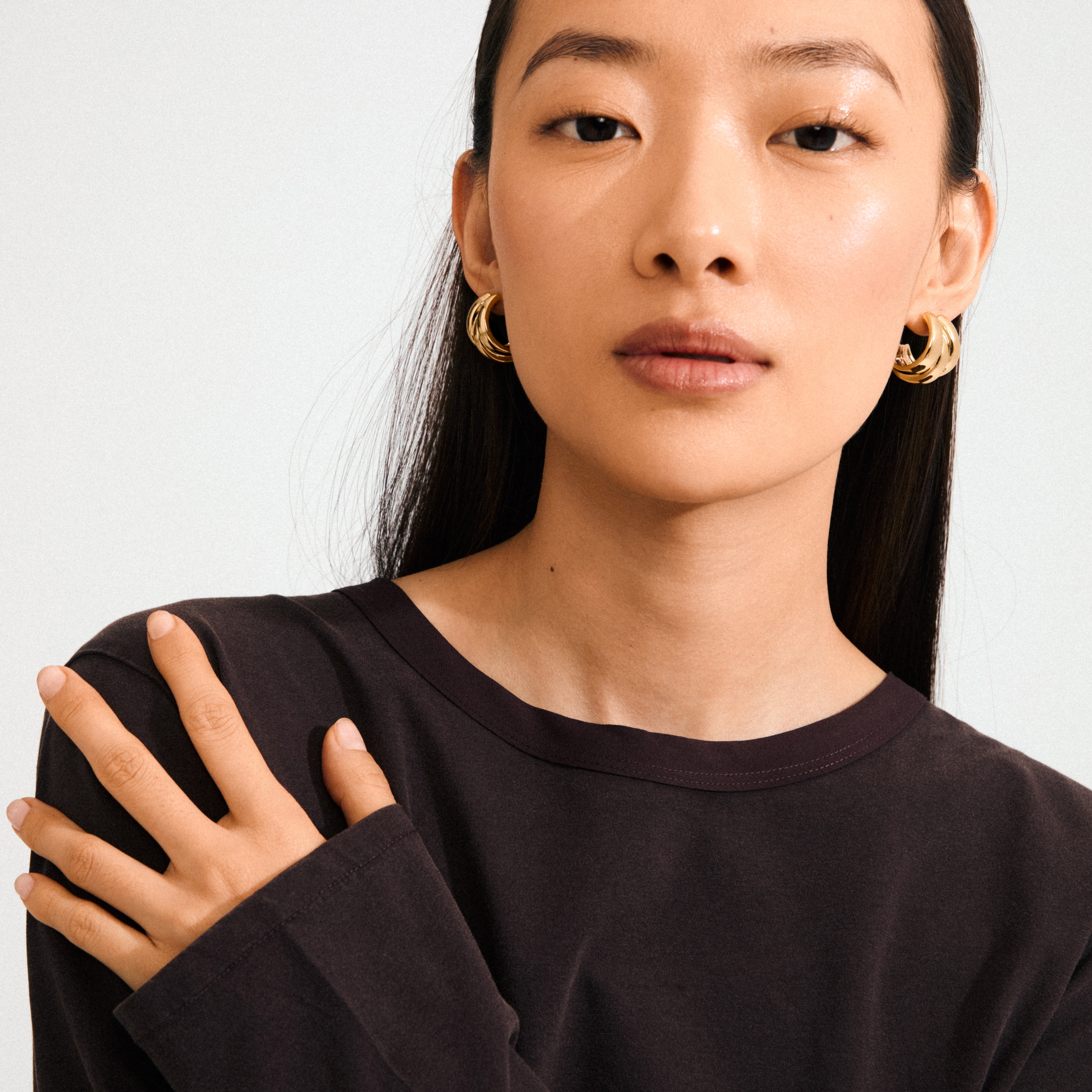 Young woman models Pilgrim's gold-plated DAMIA earrings, featuring chunky, triple-ring design for a bold statement, paired with a black top.
