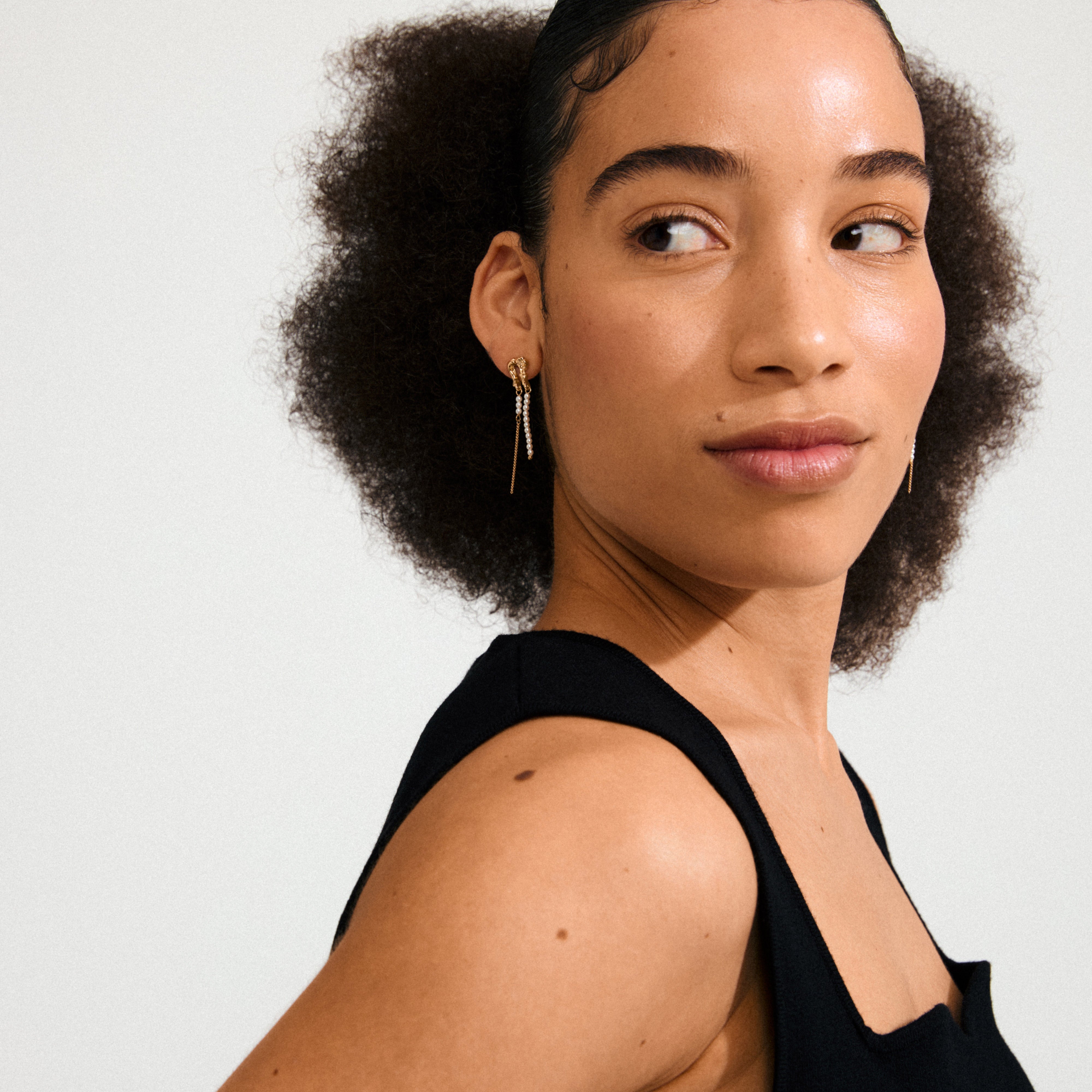 Young woman wearing Pilgrim’s VINCENT gold-plated earrings with pearl-toned beads, showcasing their enchanting, fluid design against a light backdrop.