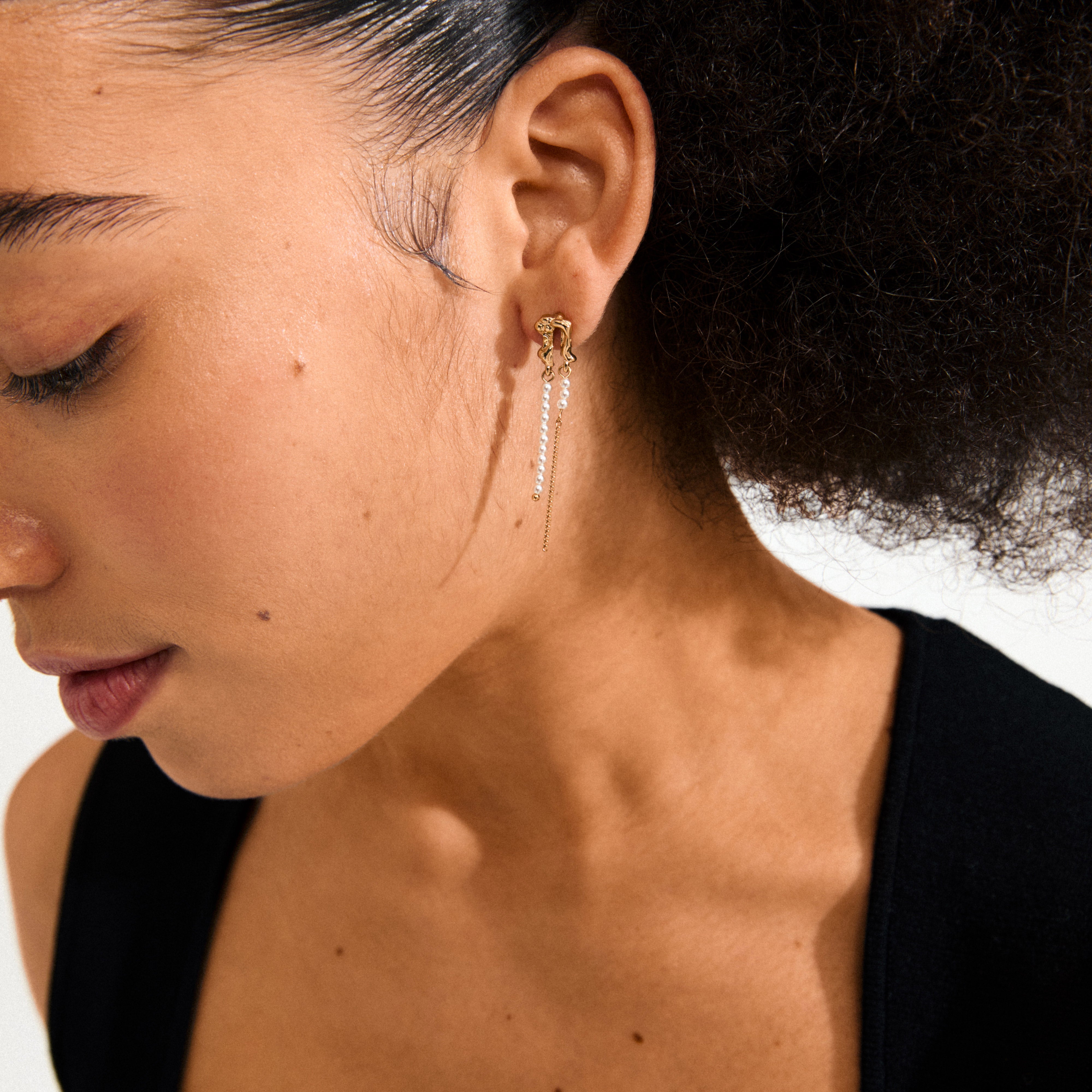 Profile view showcasing Pilgrim's VINCENT earrings, gold-plated with pearl-toned beads and a delicate chain, exemplifying Scandinavian elegance and enchanting, fluid style.