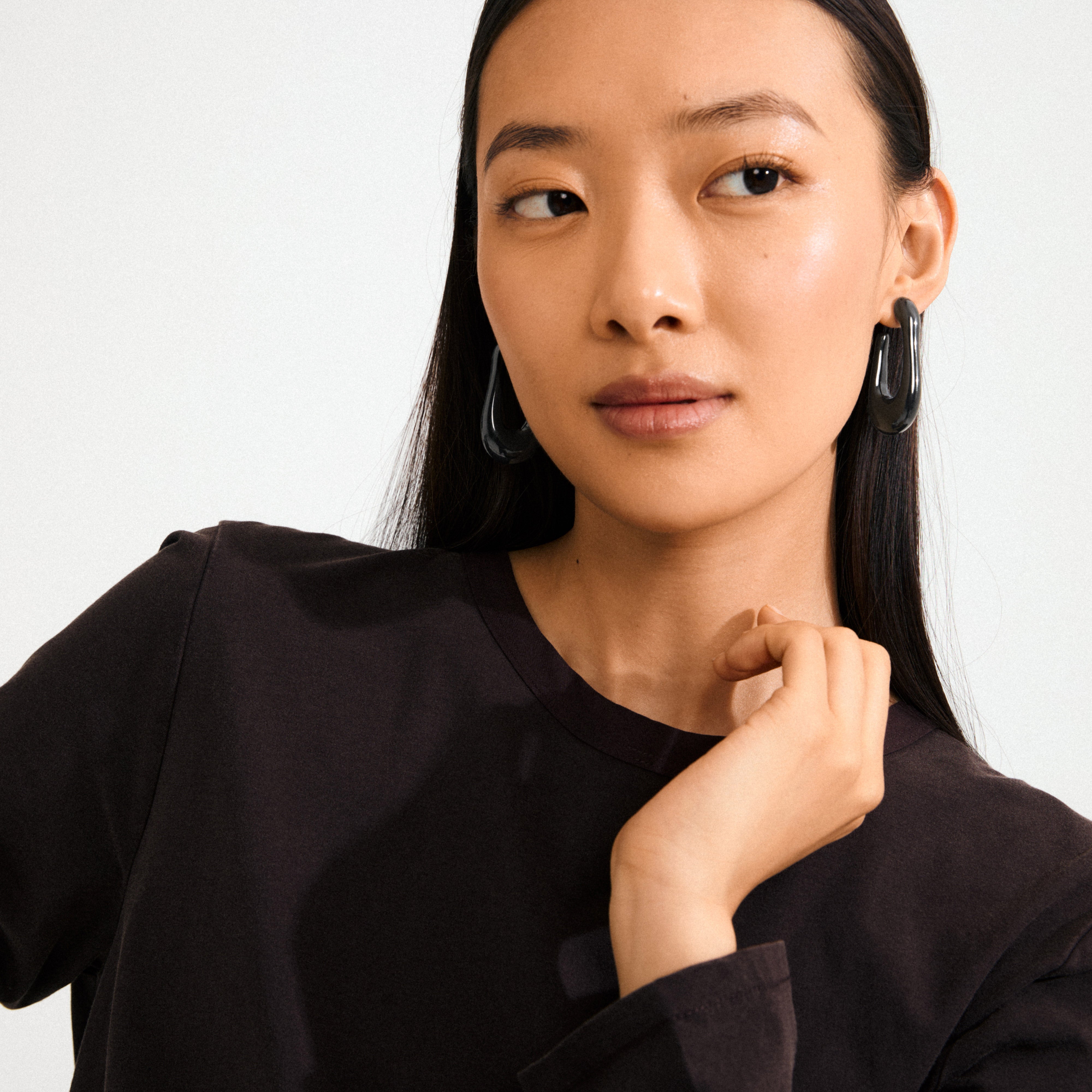 Young woman wearing ELIJAH earrings in black recycled acrylic, showcasing their chunky, oval design, adding an edgy retro touch to her simple style.