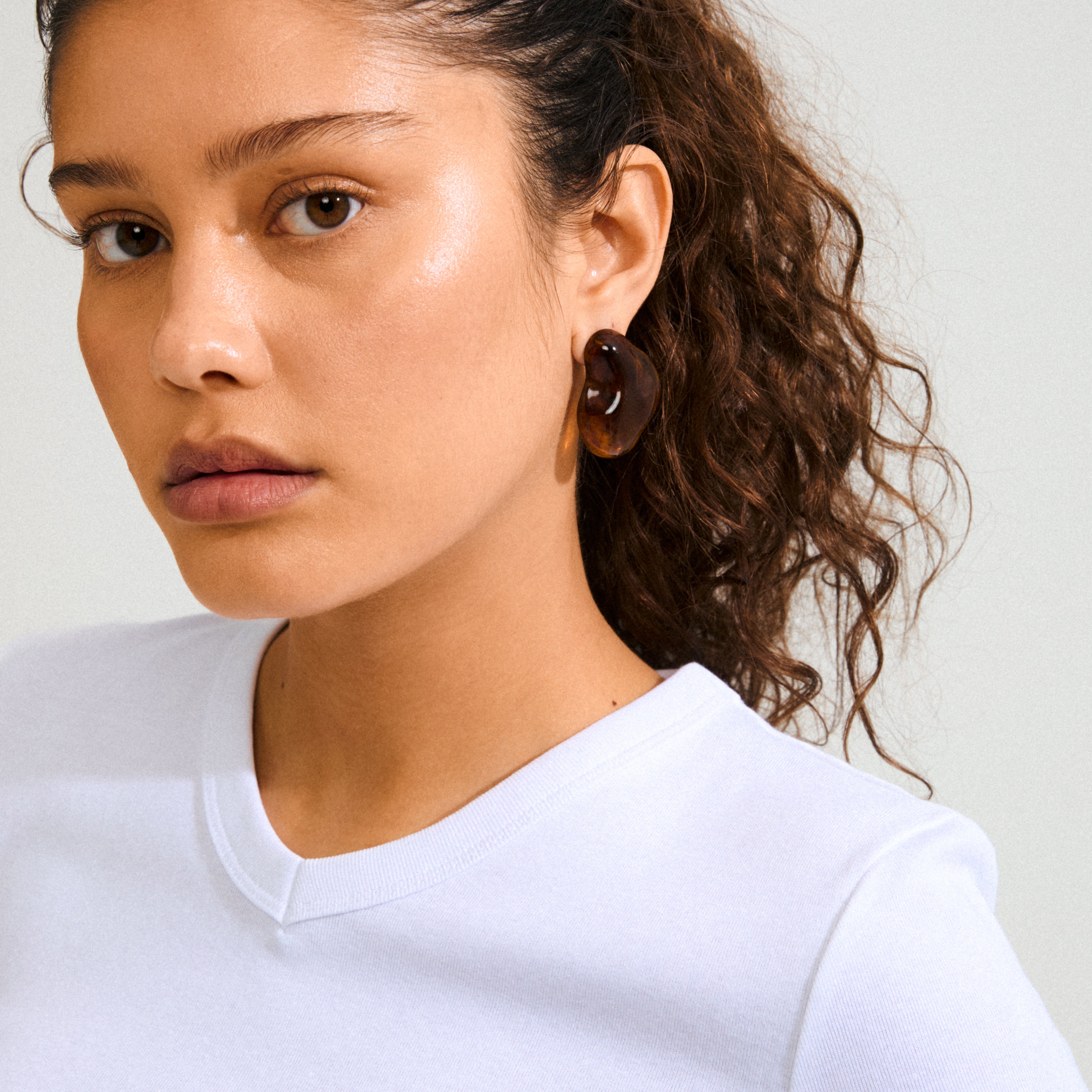 Young woman wearing Pilgrim's LIAN earrings, featuring a chunky tortoiseshell-style hoop in deep brown recycled acrylic, showcasing bold, lava-inspired design for standout style.