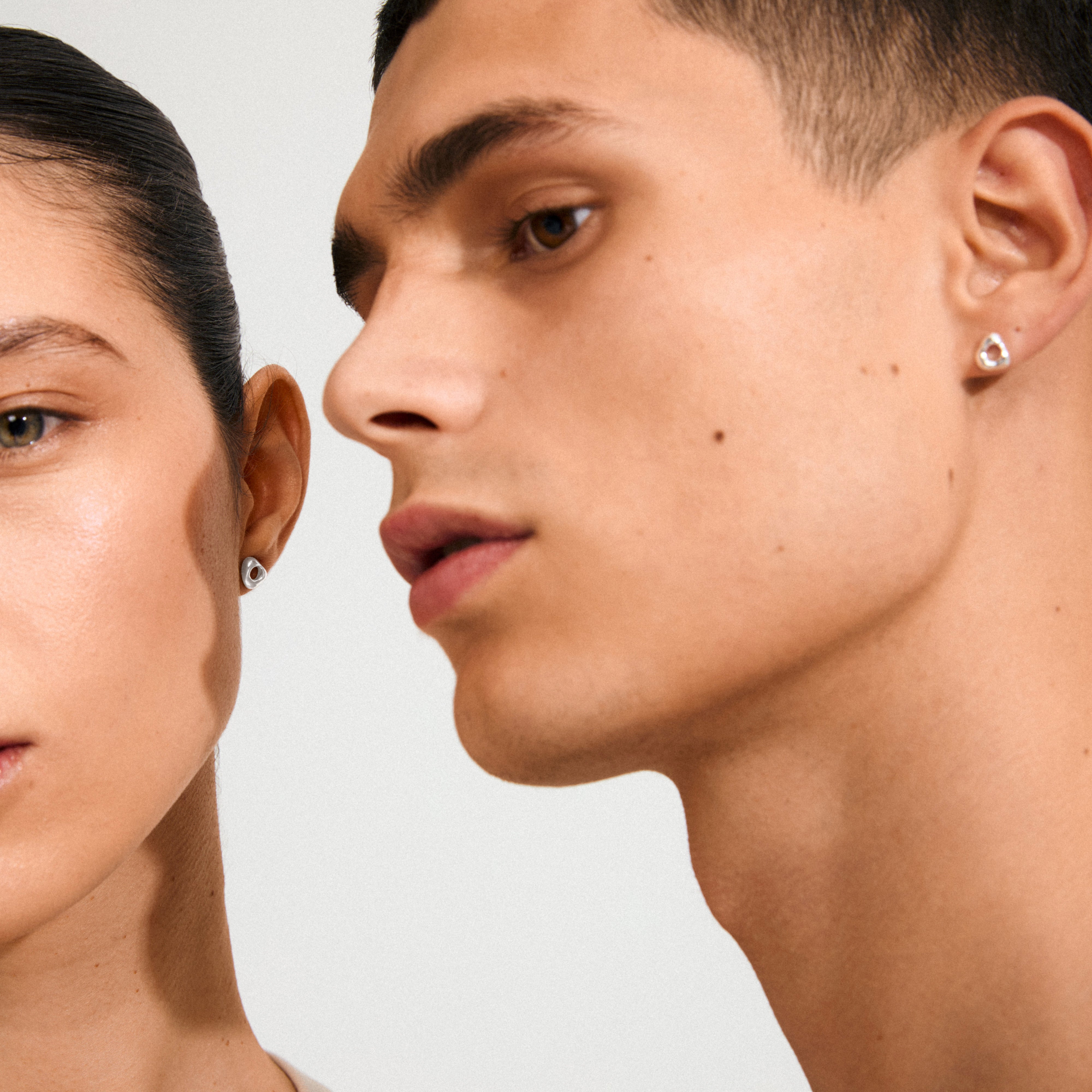 Two models wearing Pilgrim's FREE silver-plated earrings; left with teardrop-shaped stud, right with heart-shaped gemstone stud, showcasing minimalist, versatile design.