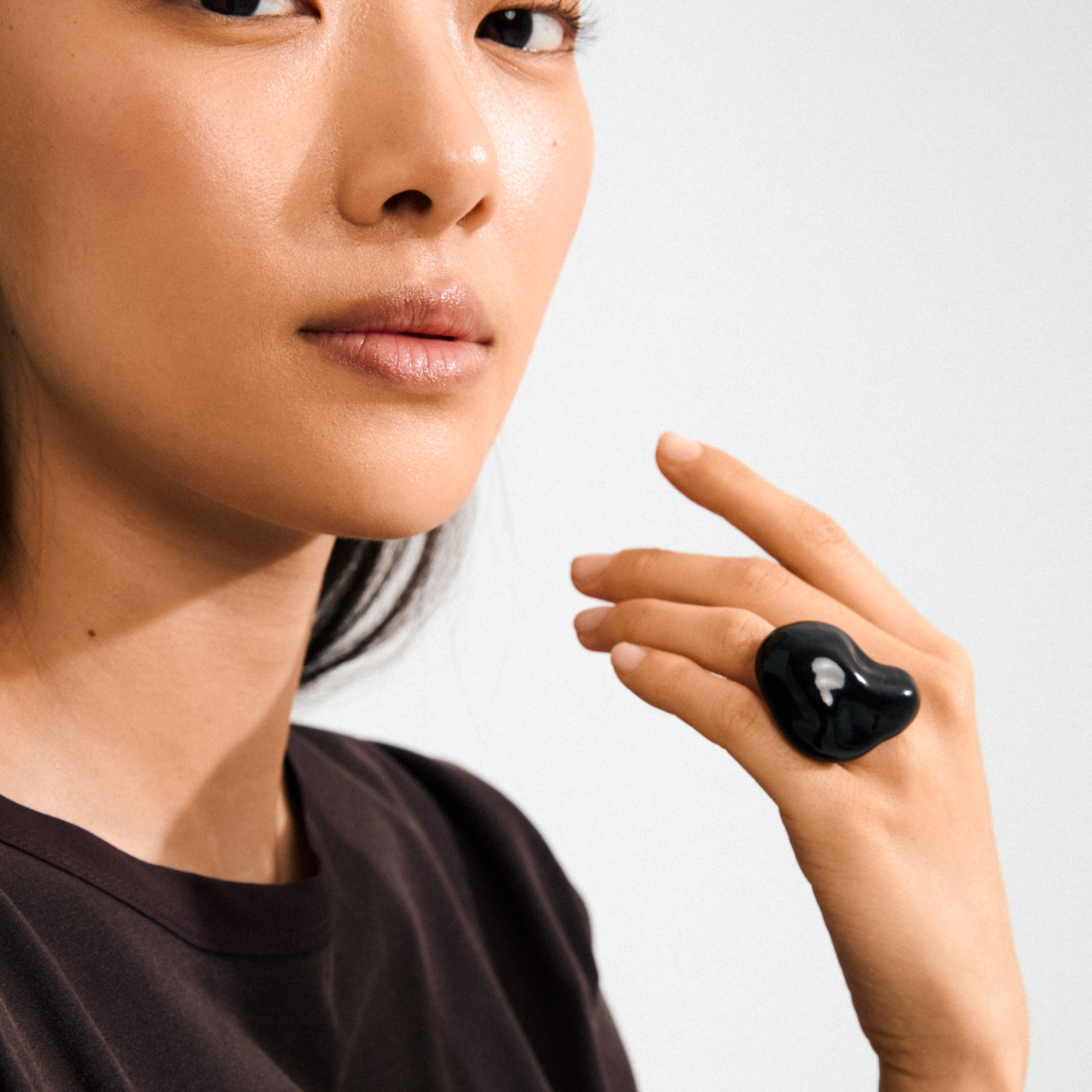 Young woman wearing the LIAN ring, a silver-plated, black acrylic statement piece from Pilgrim, showcasing its chunky, organic design on her middle finger.