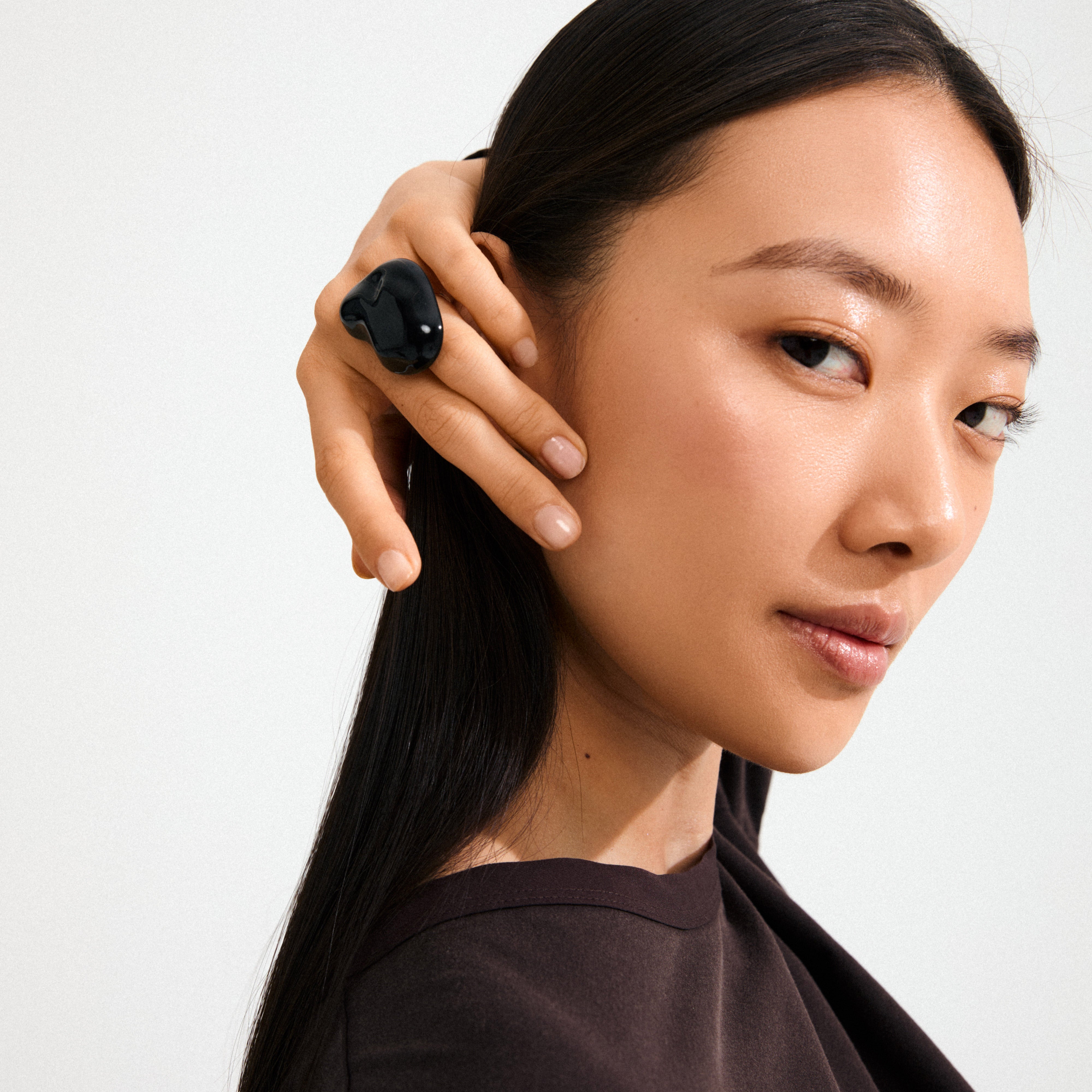 Young woman models the LIAN ring, a silver-plated, black, chunky statement piece by Pilgrim, highlighting its organic design with a sculptural, molten lava-inspired look.