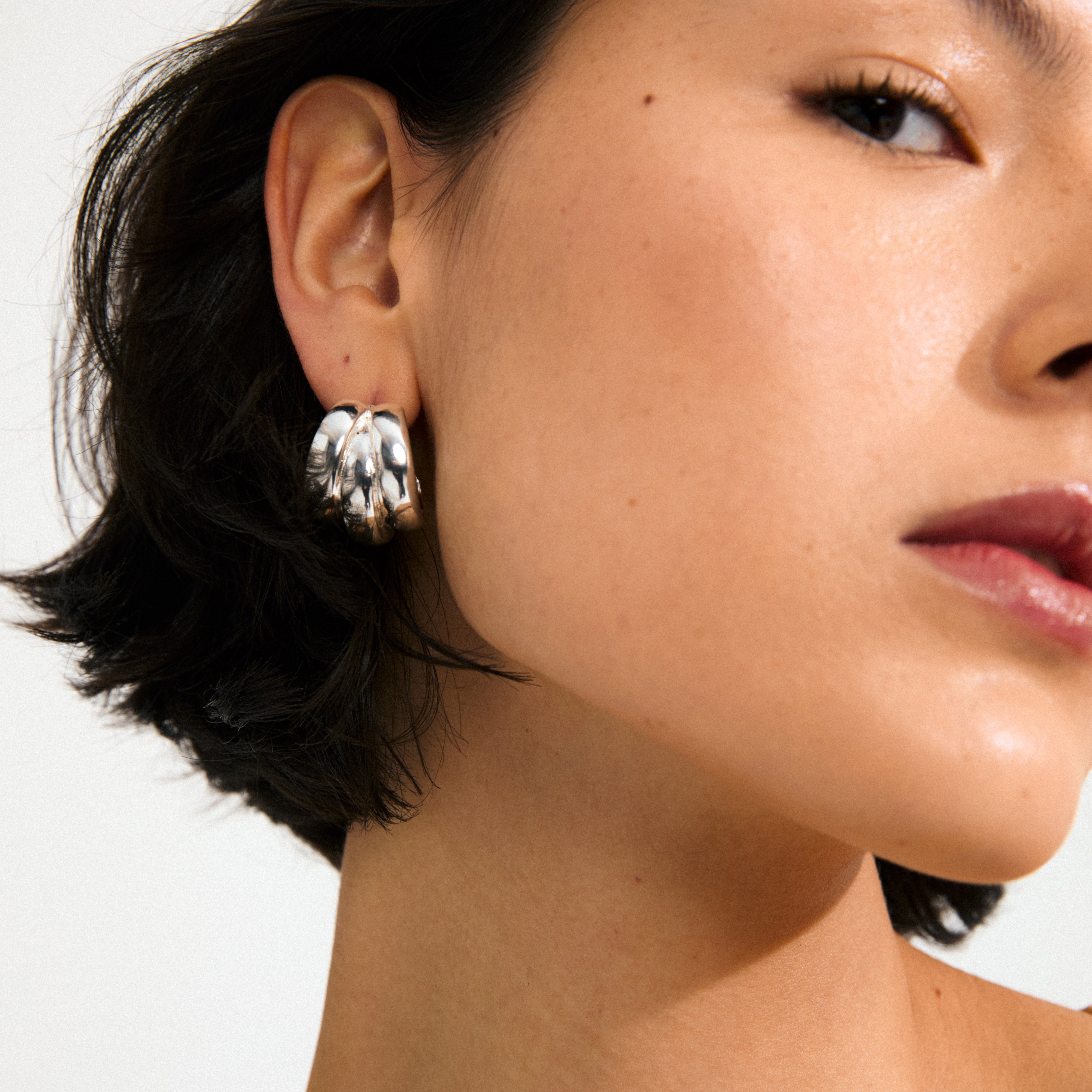 Close-up of DAMIAN silver-plated earrings from Pilgrim, showcasing a chunky, multi-band hoop design on a person's ear, perfect for a bold, stylish look.
