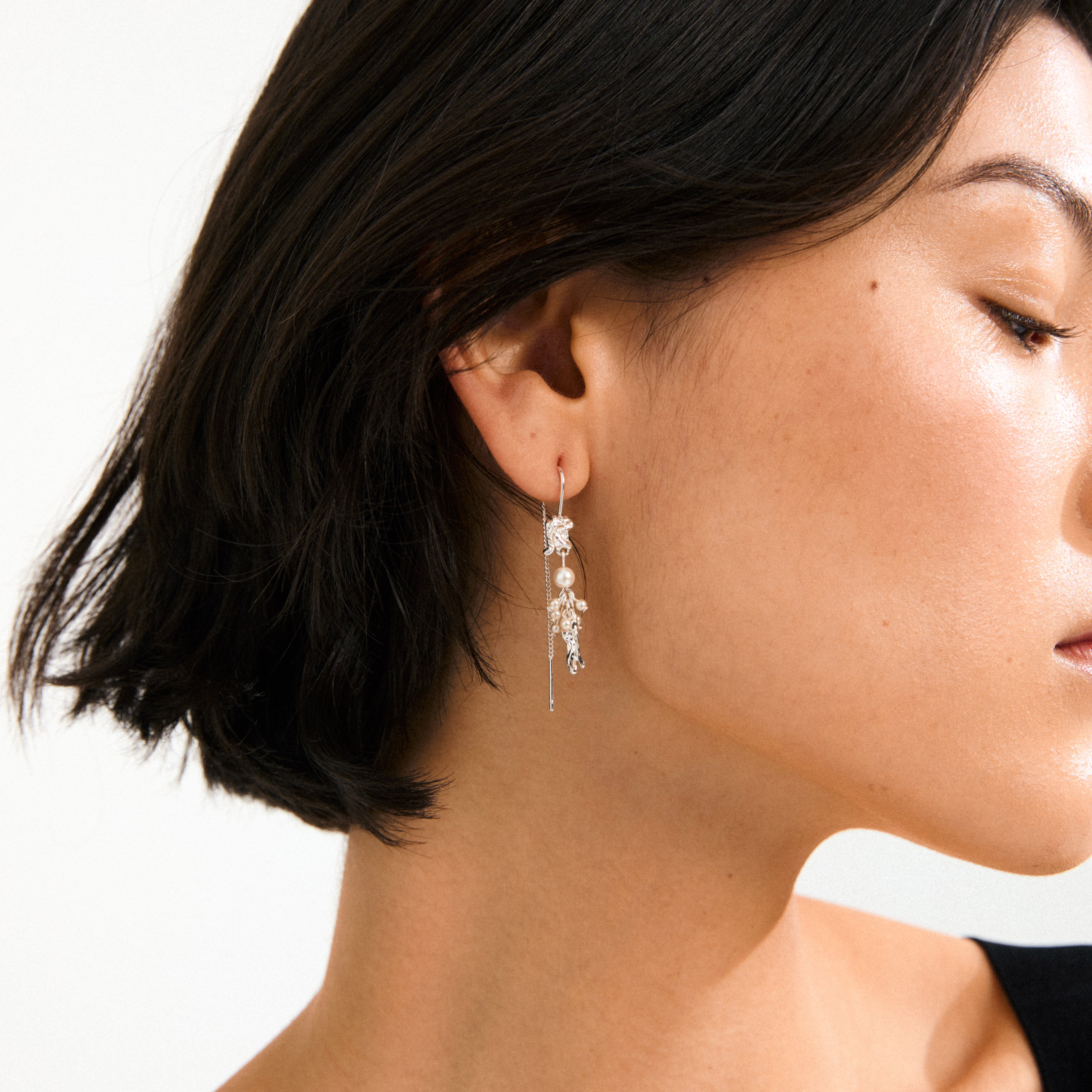 Close-up of a woman's ear adorned with Pilgrim's MILO chain earrings, silver-plated with dangling chains, sculptural elements, and a single pearl, embodying a whimsical, adventurous style.