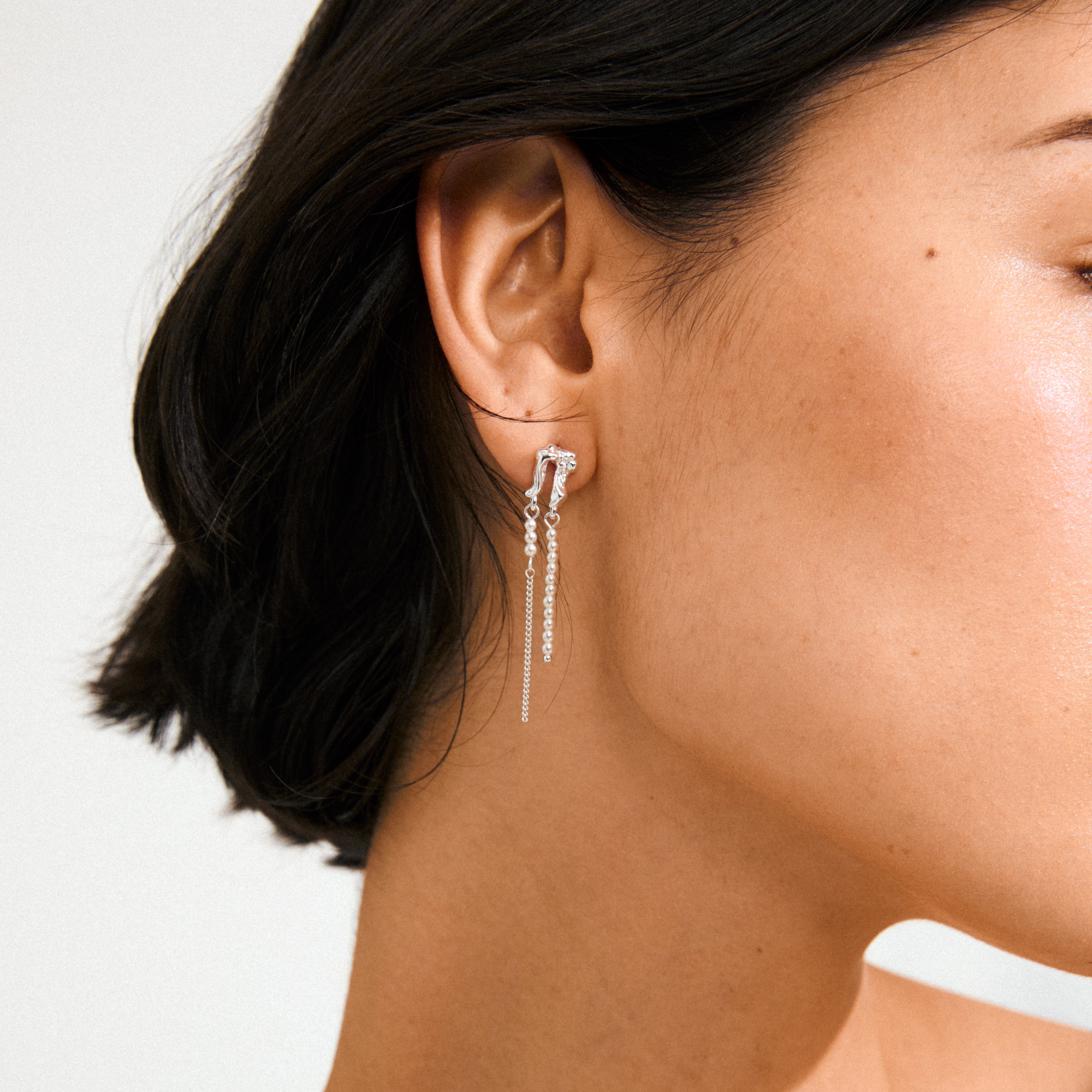 Close-up of ear wearing VINCENT earrings silver-plated from Pilgrim, featuring a knotted cluster and three delicate chains with bead accents, exuding fairytale elegance.