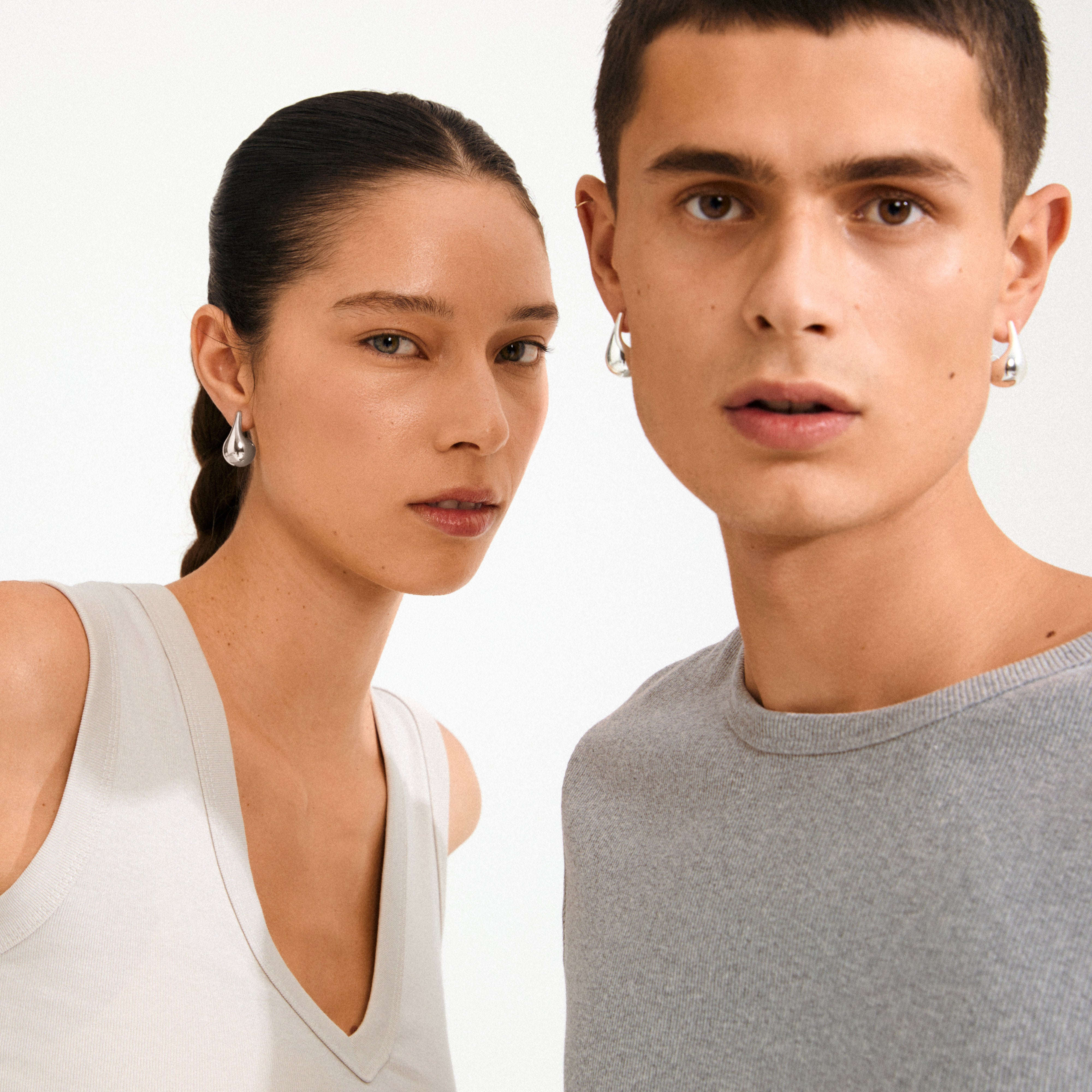 Two young adults wearing Pilgrim's silver-plated JUNIPER earrings, showcasing a teardrop design that reflects Scandinavian style and modern elegance.