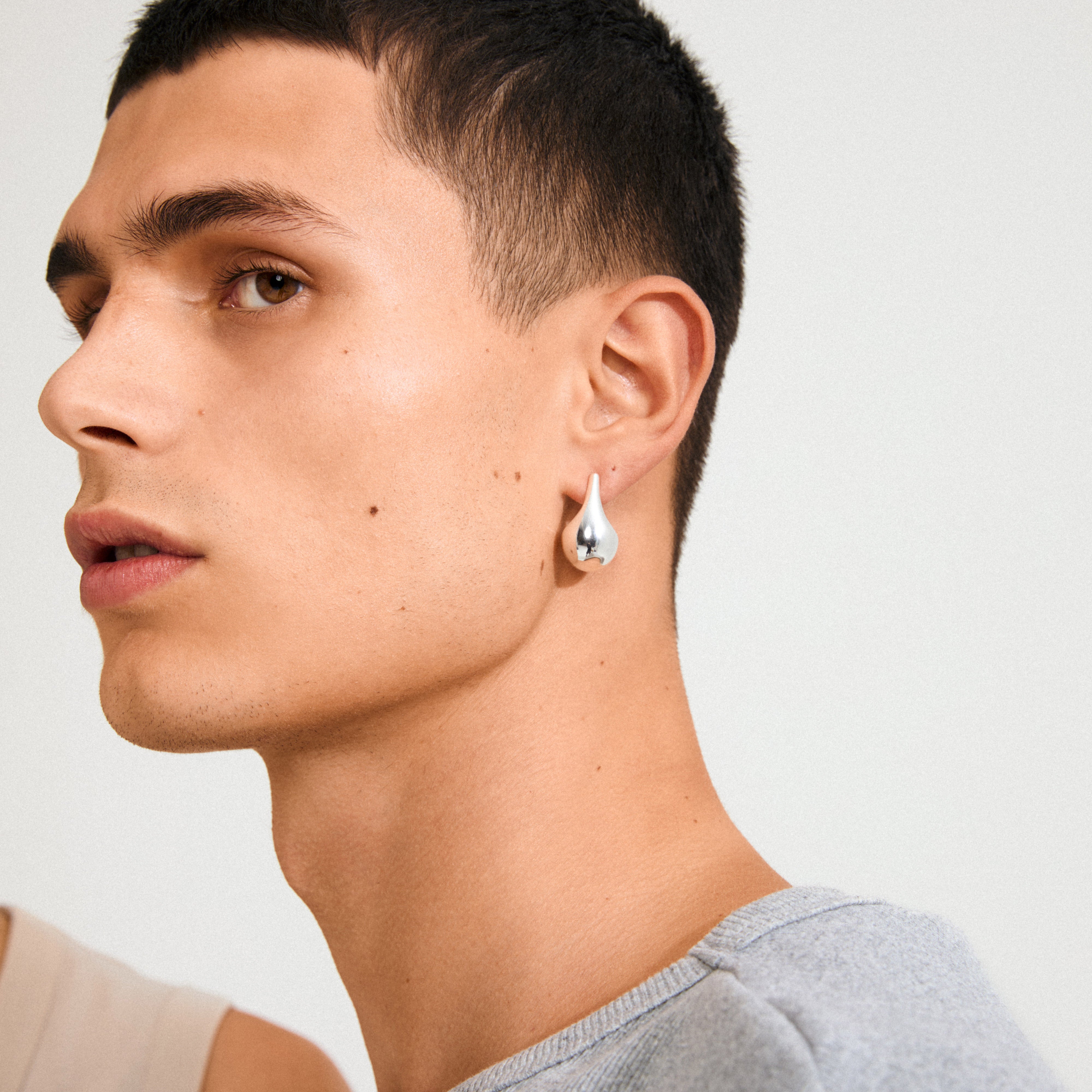 Young man wearing Pilgrim's JUNIPER silver-plated teardrop earring, showcasing its polished shine and retro Scandinavian style in a close-up side profile.