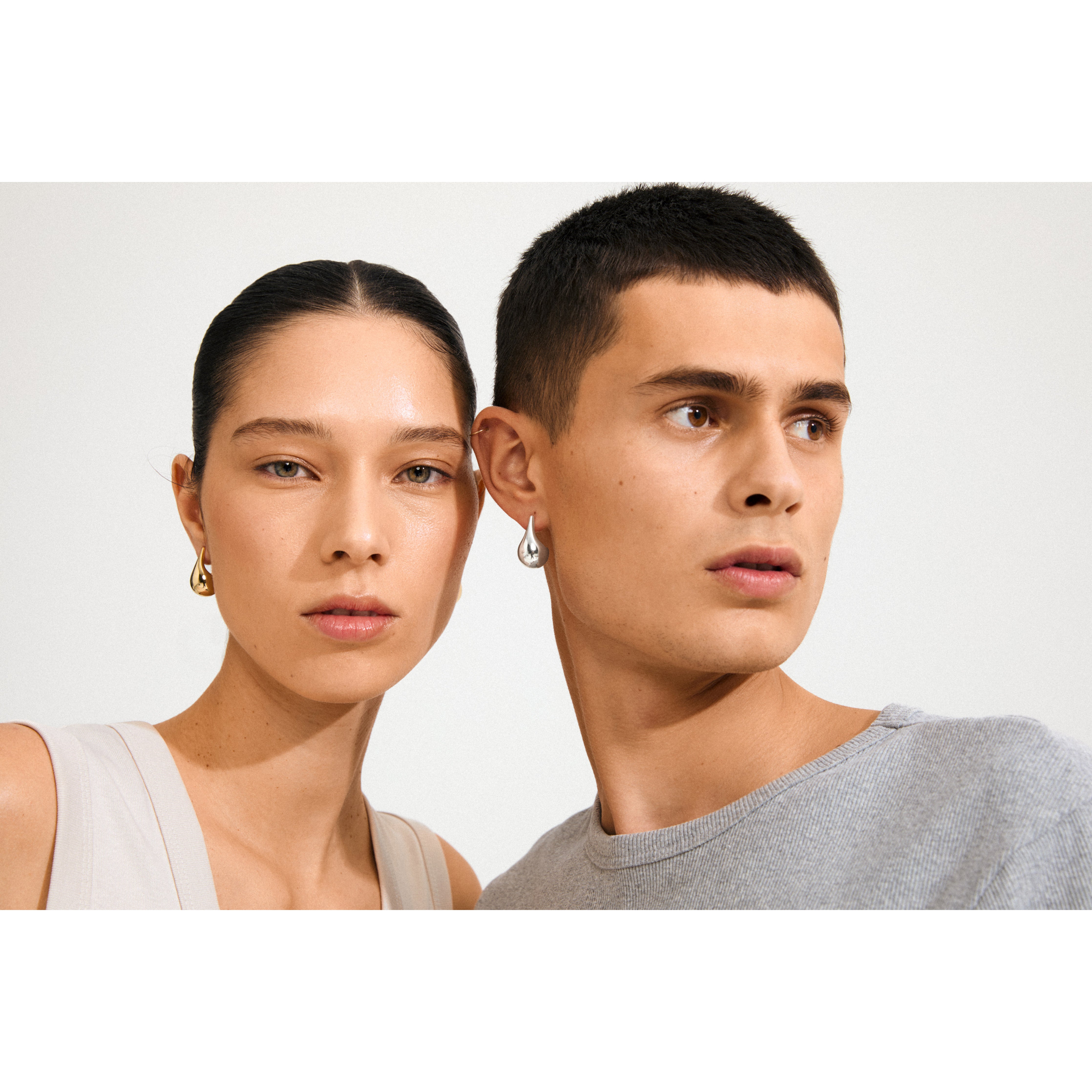 Two models wearing Pilgrim's JUNIPER earrings, showcasing the teardrop design in gold and silver finishes, emphasizing Scandinavian-inspired style and sustainability.
