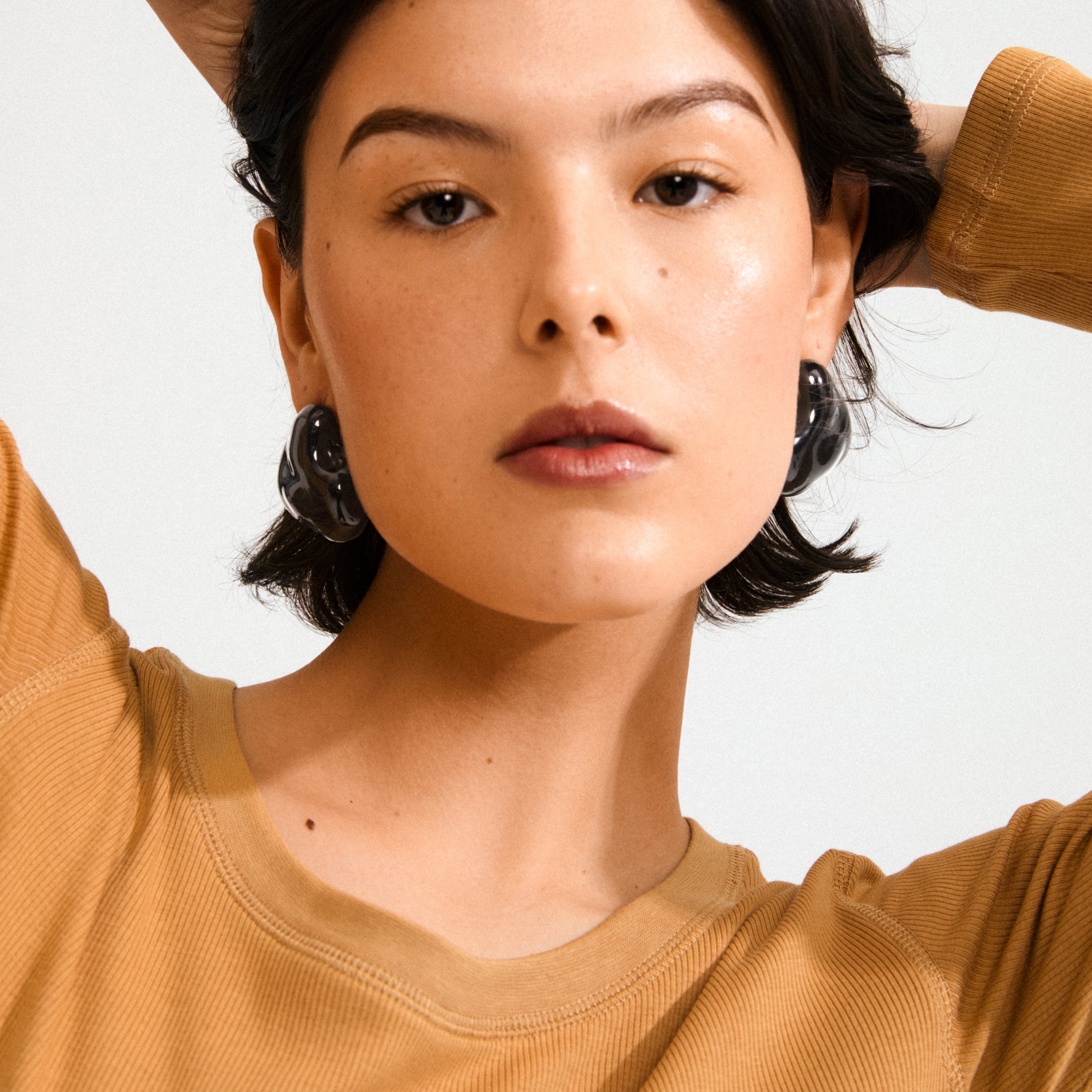 Young woman wearing LIAN earrings in black, showcasing their bold, fluid design. Her short dark hair and camel top accentuate the earrings' statement look.