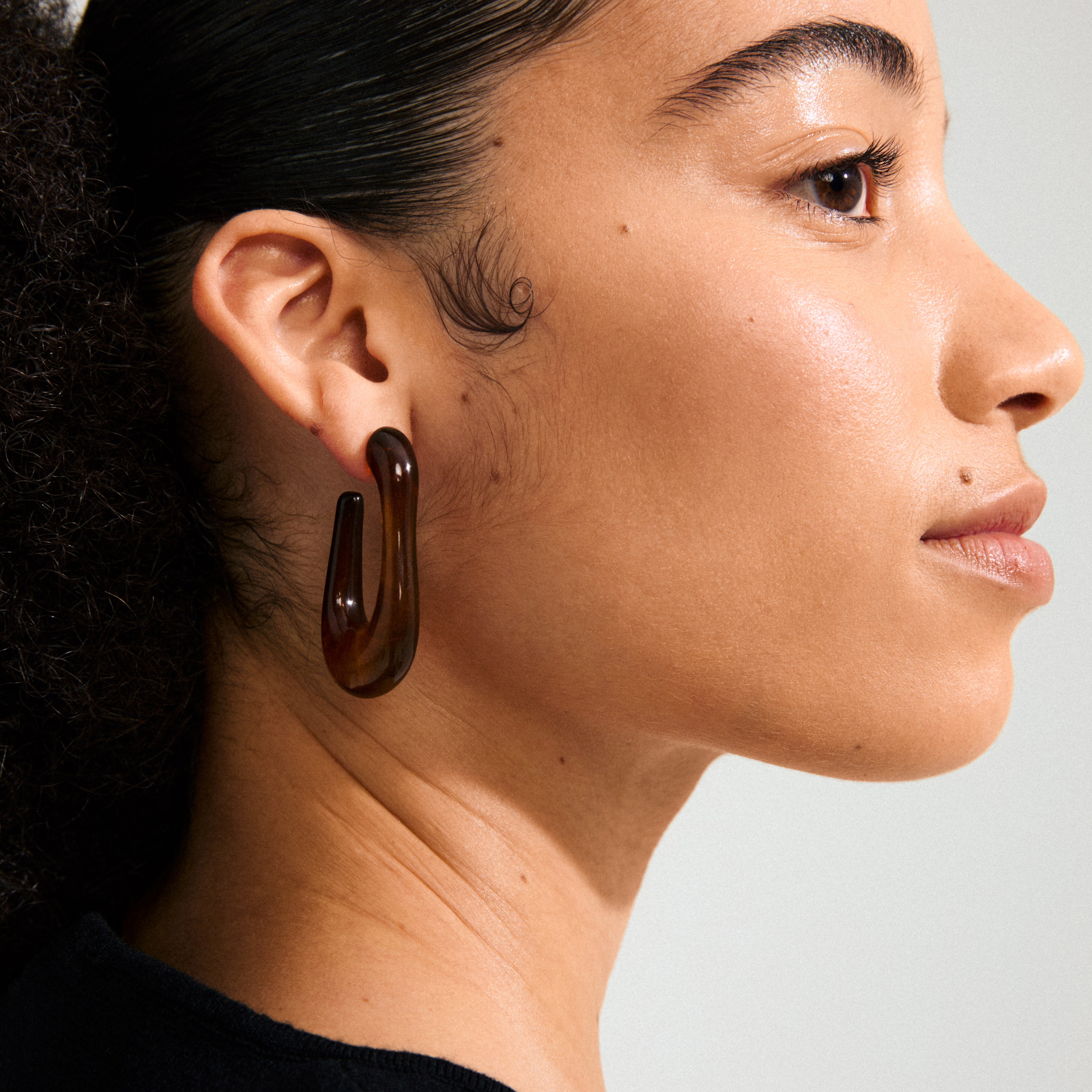 Young woman wearing ELIJAH earrings in brown recycled resin, featuring an abstract hook shape, highlighting Pilgrim's edgy, urban style with a retro influence.