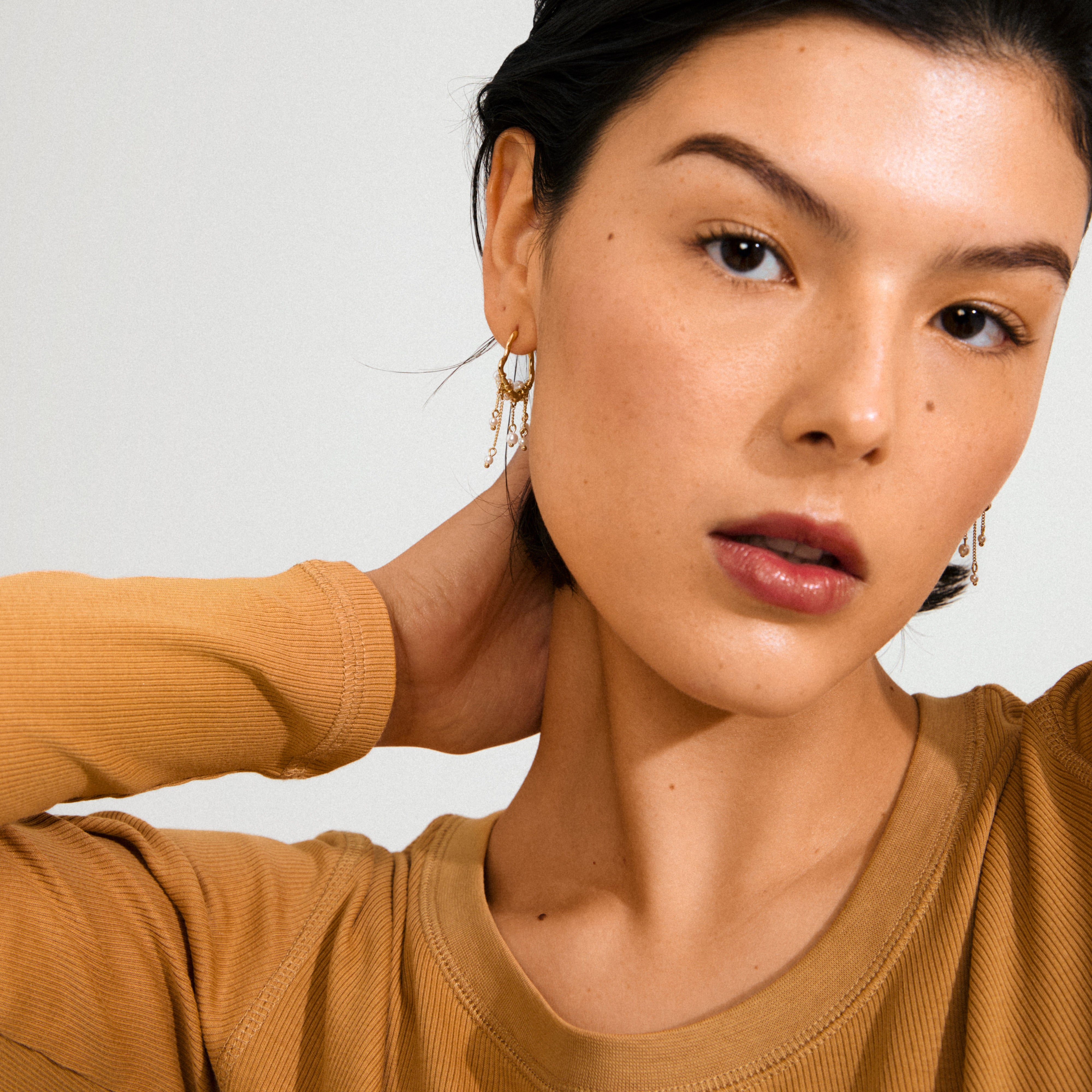 JASPER gold-plated earrings: organic, dreamcatcher-inspired, with pearls and delicate chains, worn by a young woman in a mustard ribbed top, showcasing a whimsical, boho style.