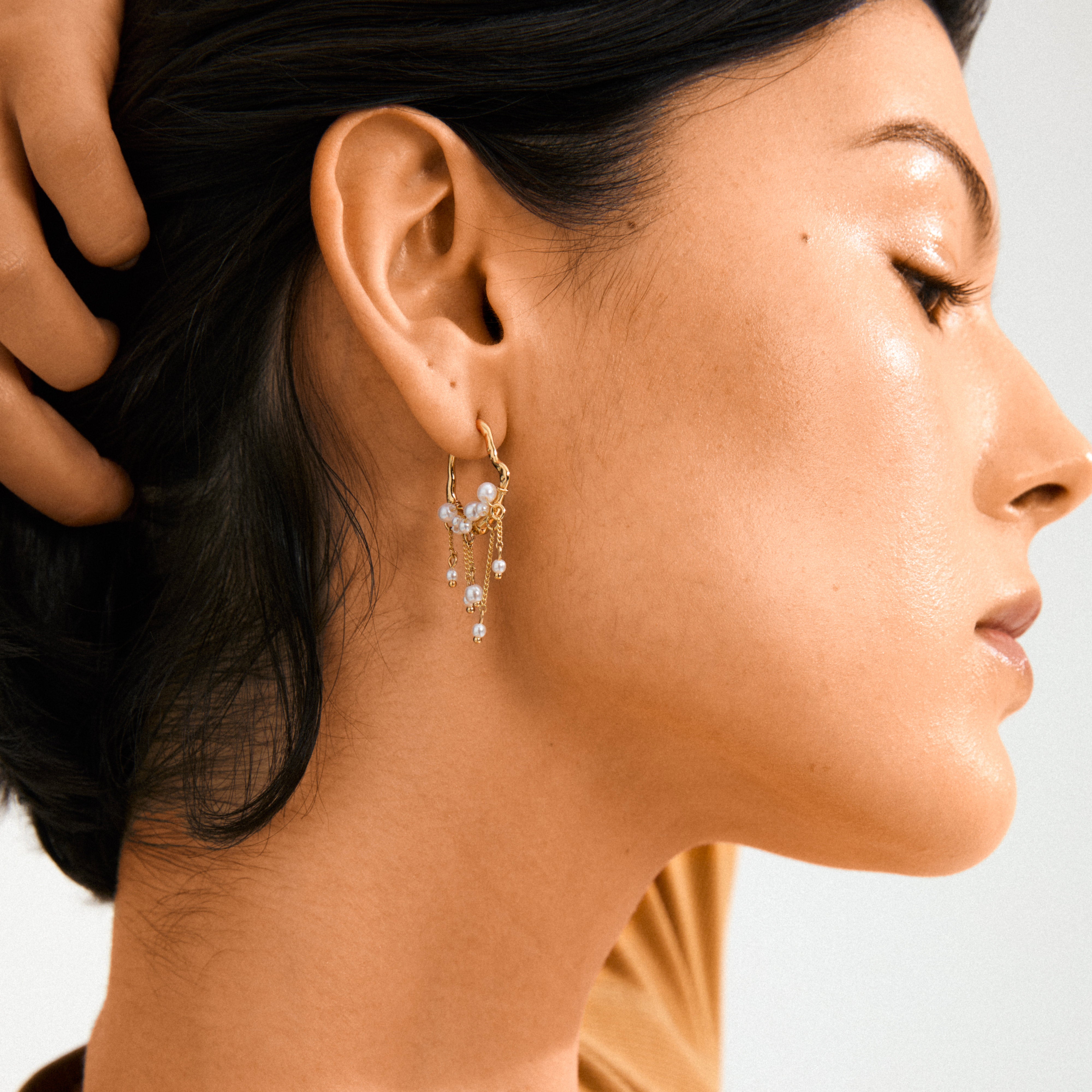The JASPER earrings gold-plated, featuring dangling chains and pearls, adorn a woman's profile, highlighting Pilgrim's whimsical and boho-inspired design.