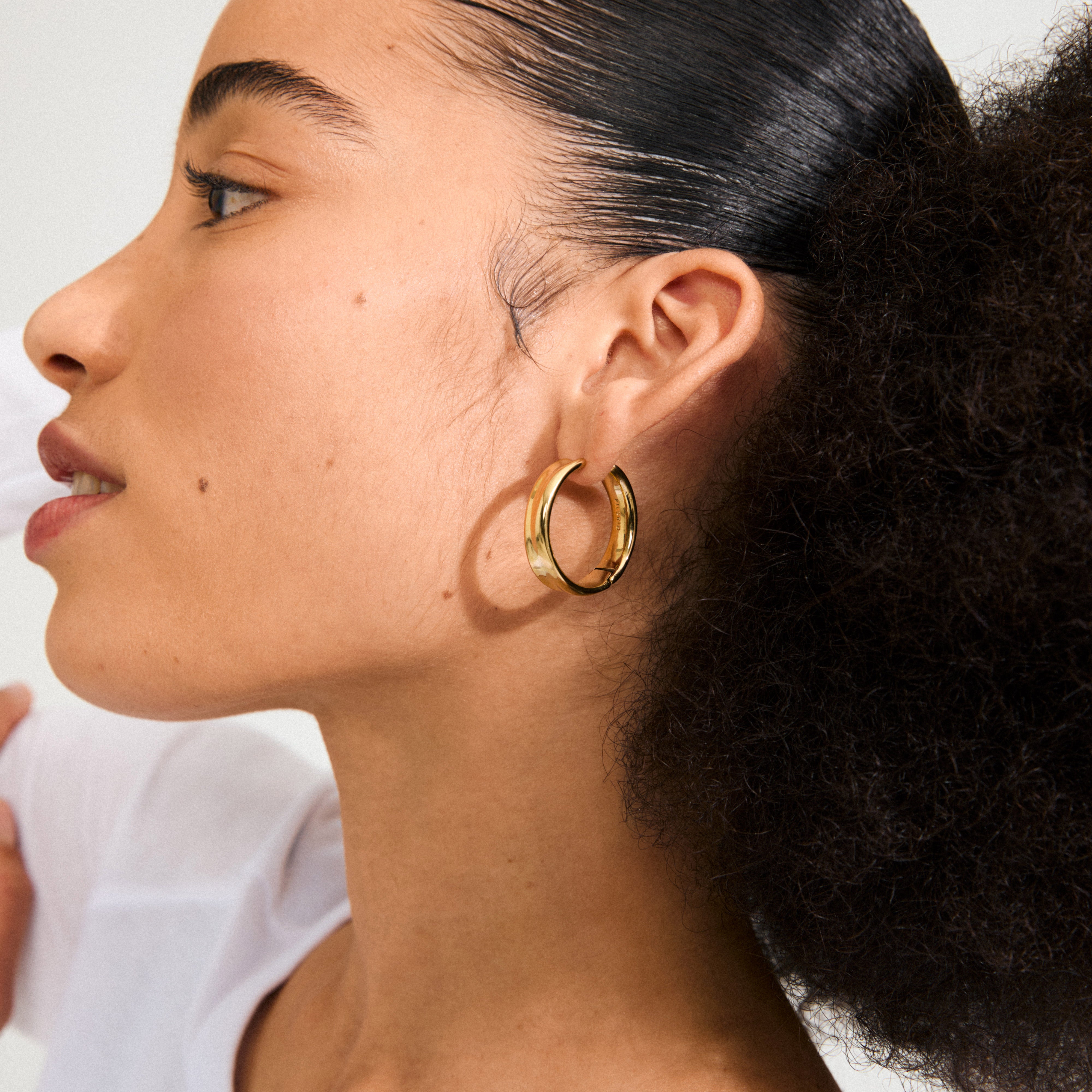 KAYDEN hoops gold-plated adorn a sleek hairstyle, showcasing their broad, shiny design—a versatile piece reflecting Scandinavian style, perfect for any occasion.