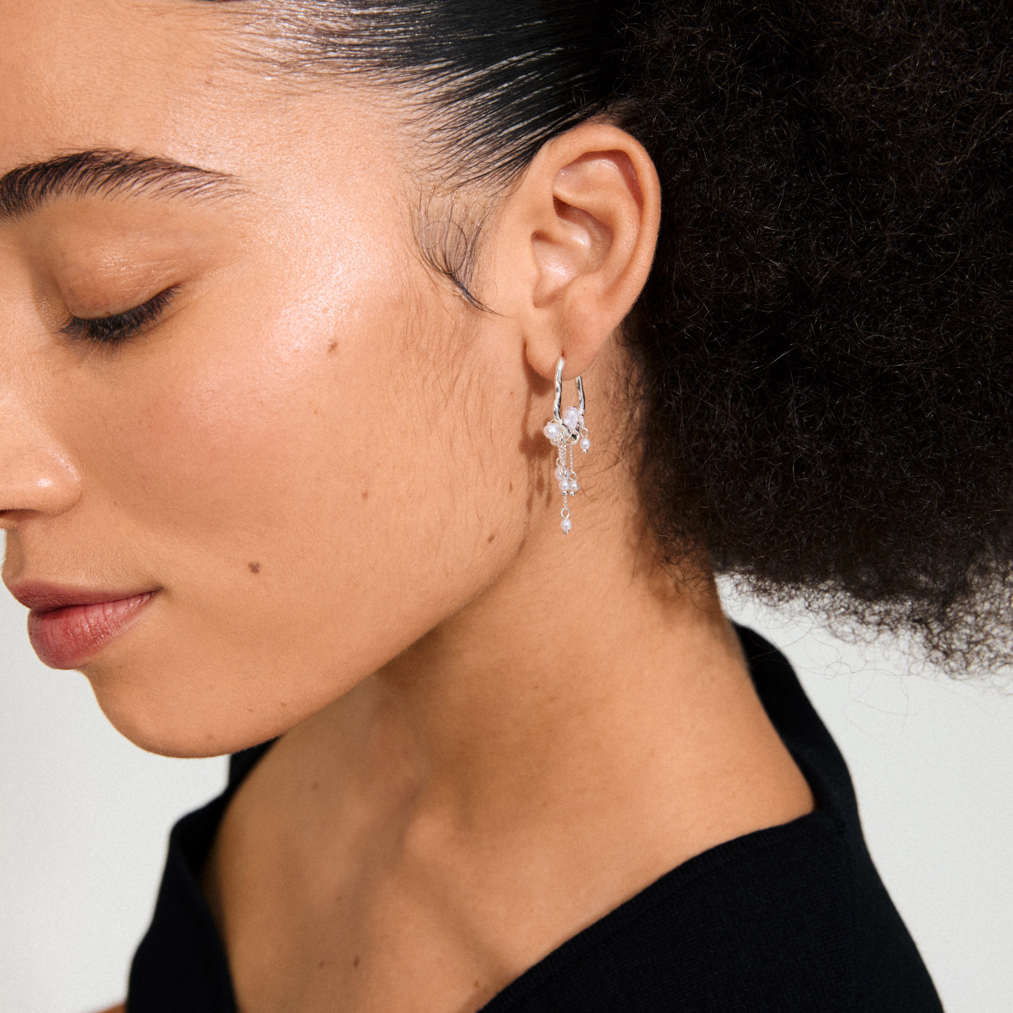 Close-up of a person wearing JASPER earrings, silver-plated hoops with beads and chains, showcasing an organic, dreamcatcher-inspired design by Pilgrim.