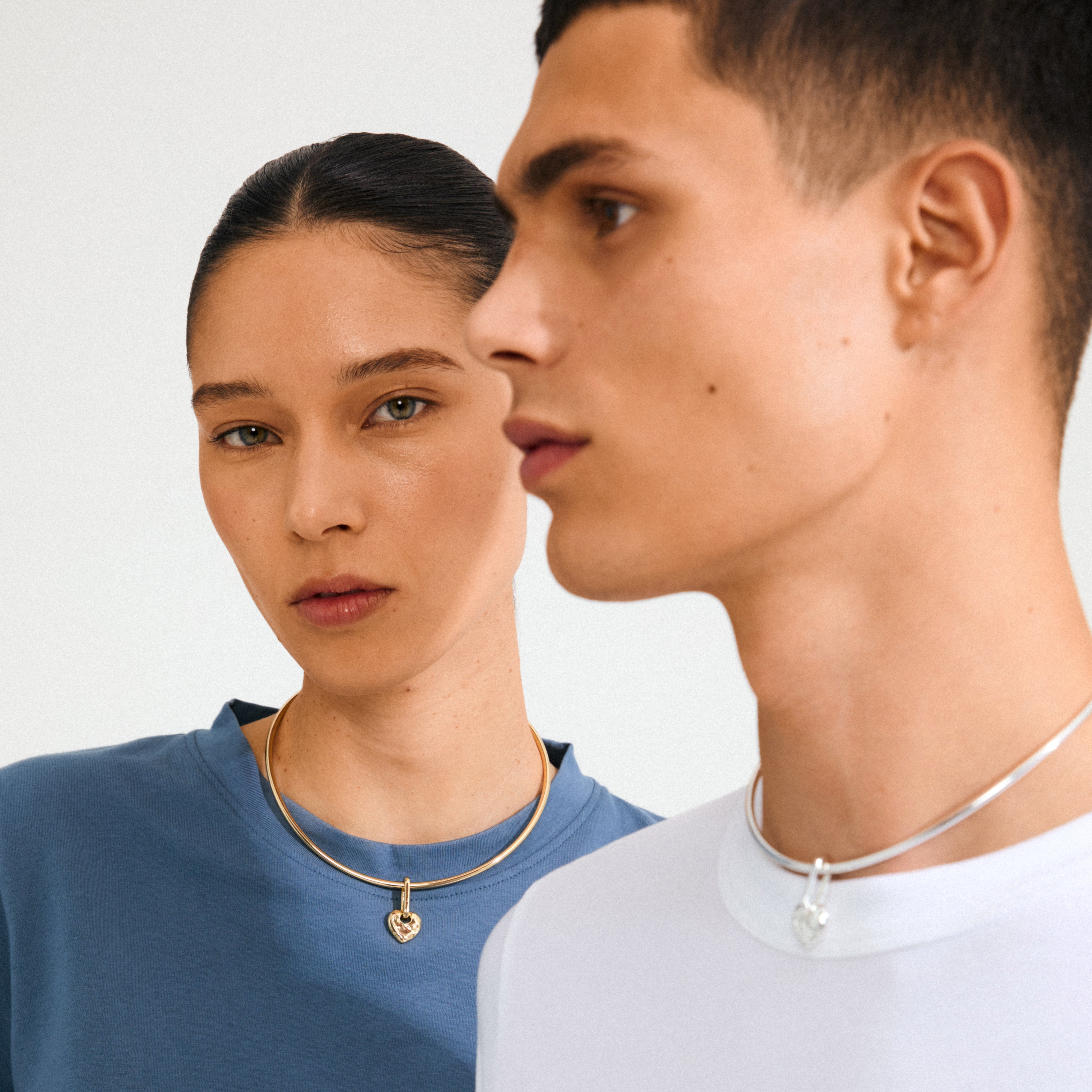 Two models wearing minimalist chokers featuring Pilgrim's CHARM rough heart pendant, silver-plated, showcasing recycled, Scandinavian-inspired design for individualistic, eco-conscious style.